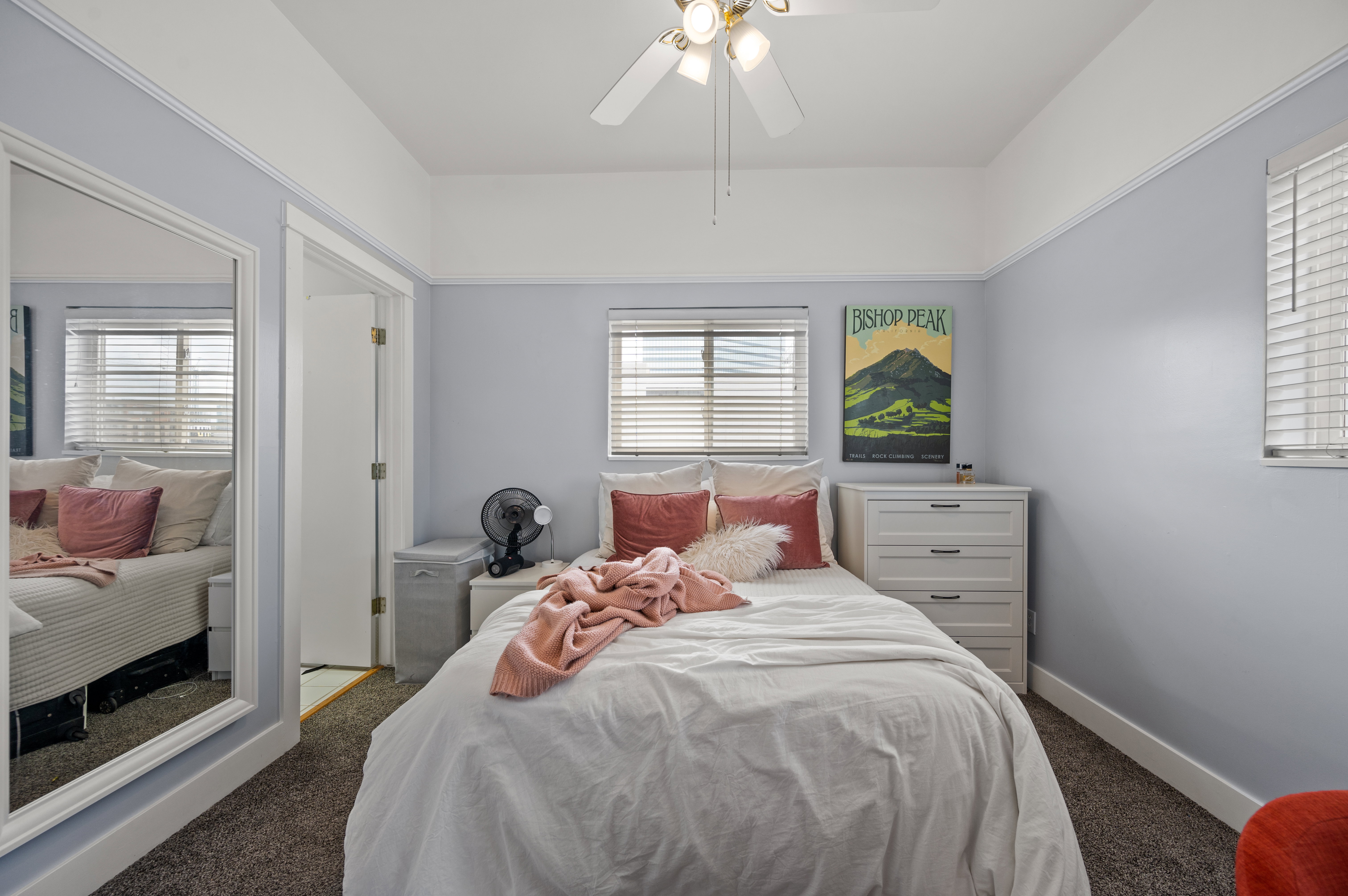 Carpeted room featuring a ceiling fan with integrated lighting, multiple windows with blinds, and a mirrored closet door
