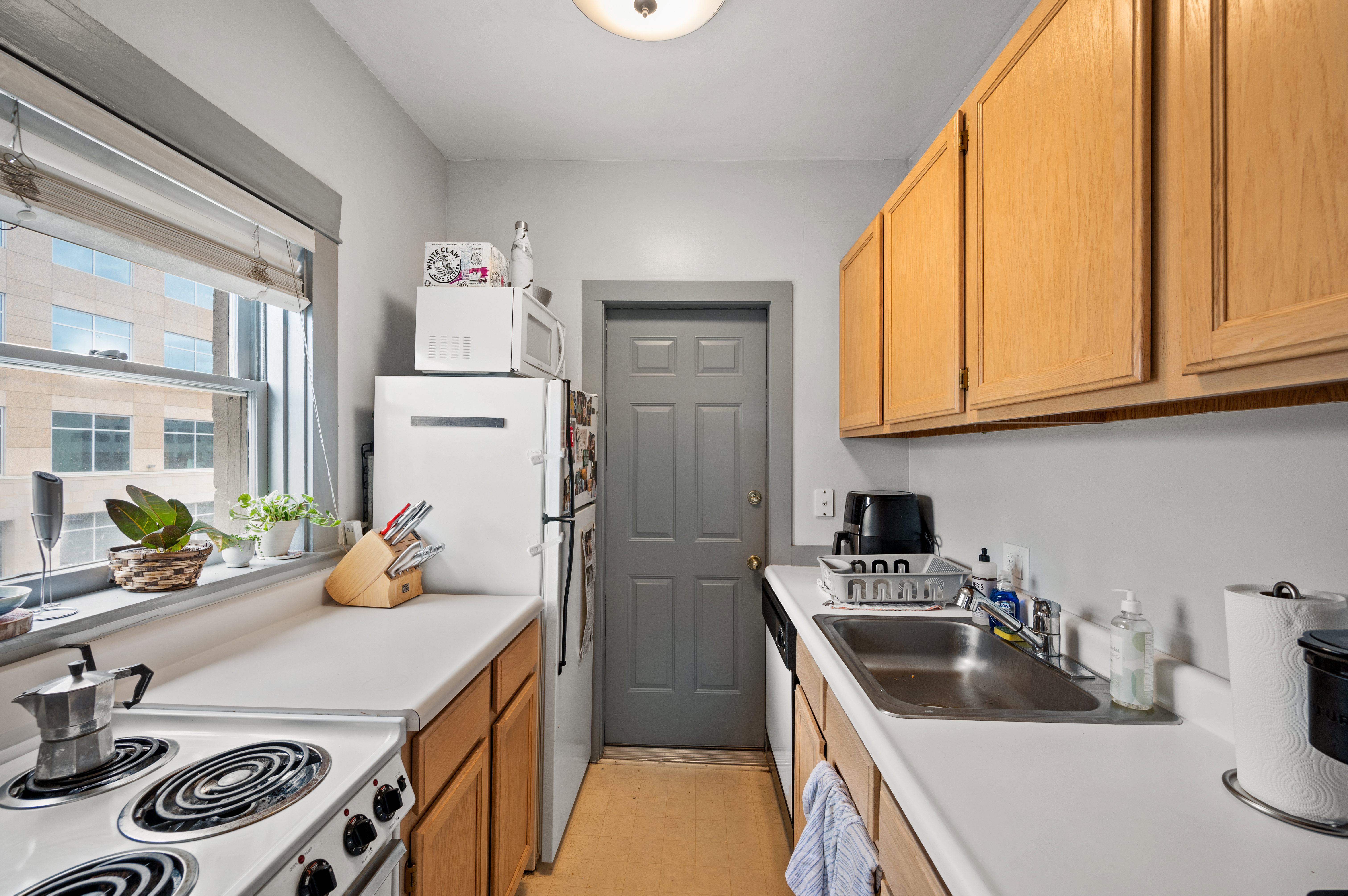 Galley kitchen featuring light wood-finish cabinetry, white countertops, and a stainless steel sink