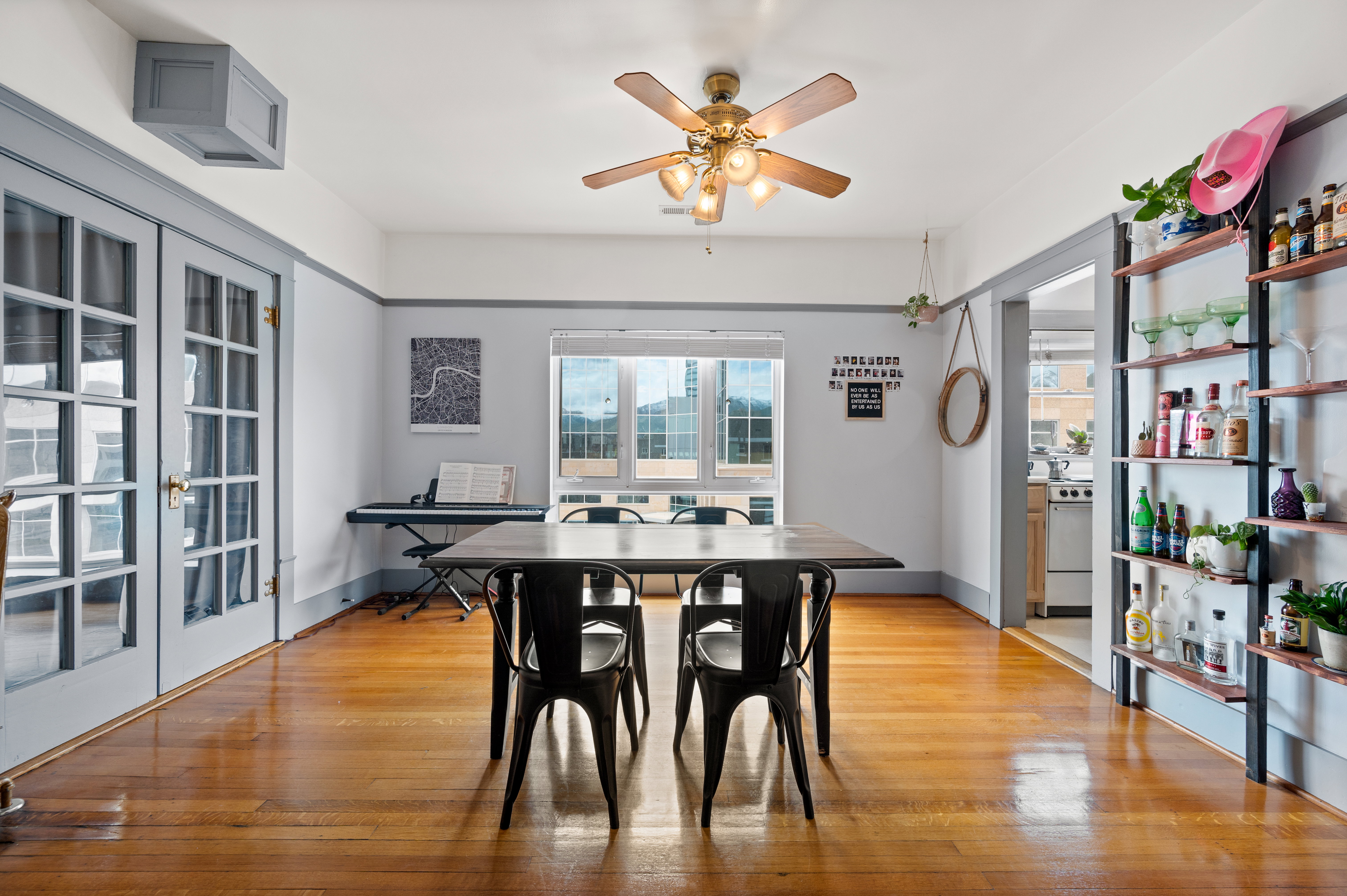 Dining area featuring wood-finish flooring, a ceiling fan with integrated lighting, window-paned double doors, built-in shelving, and large windows