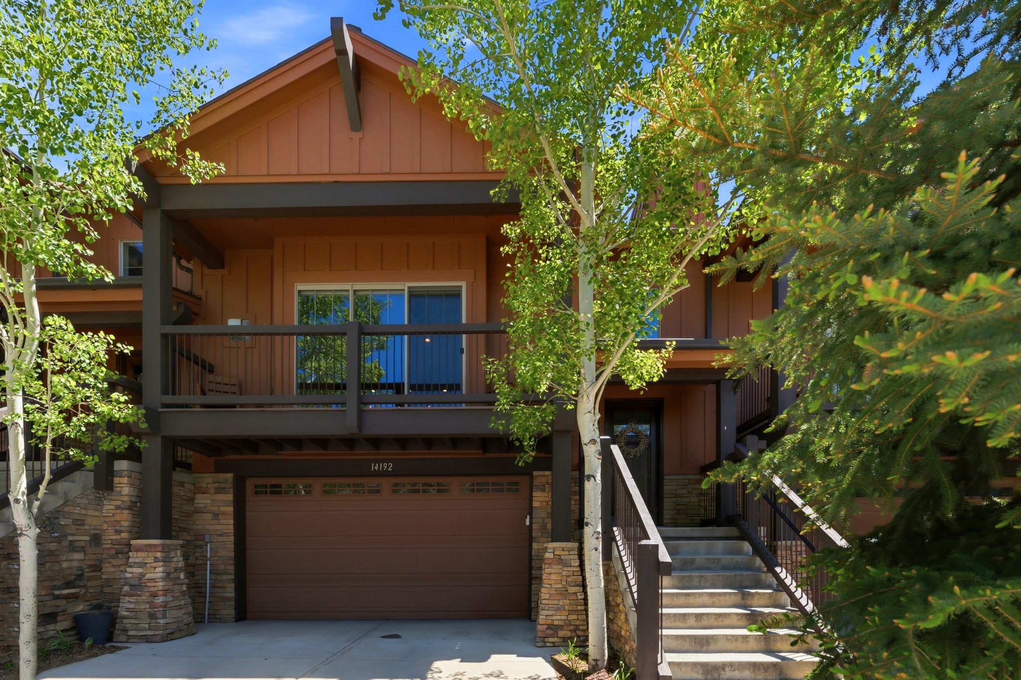 Multi-level residence featuring a brown siding exterior, stone accents, and a prominent front-facing garage with a brown door