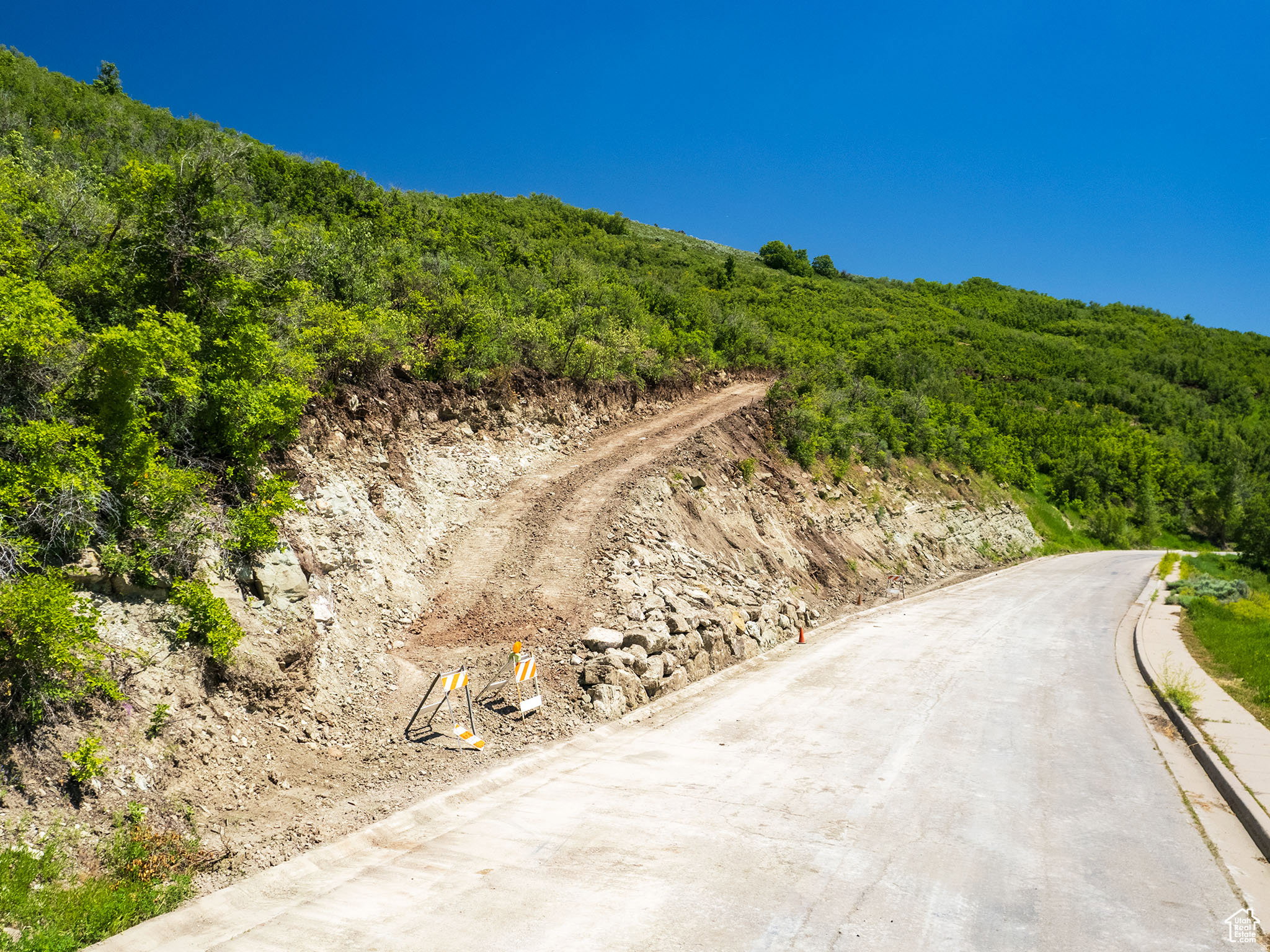 Paved road extending into a verdant hillside with a prepared building site