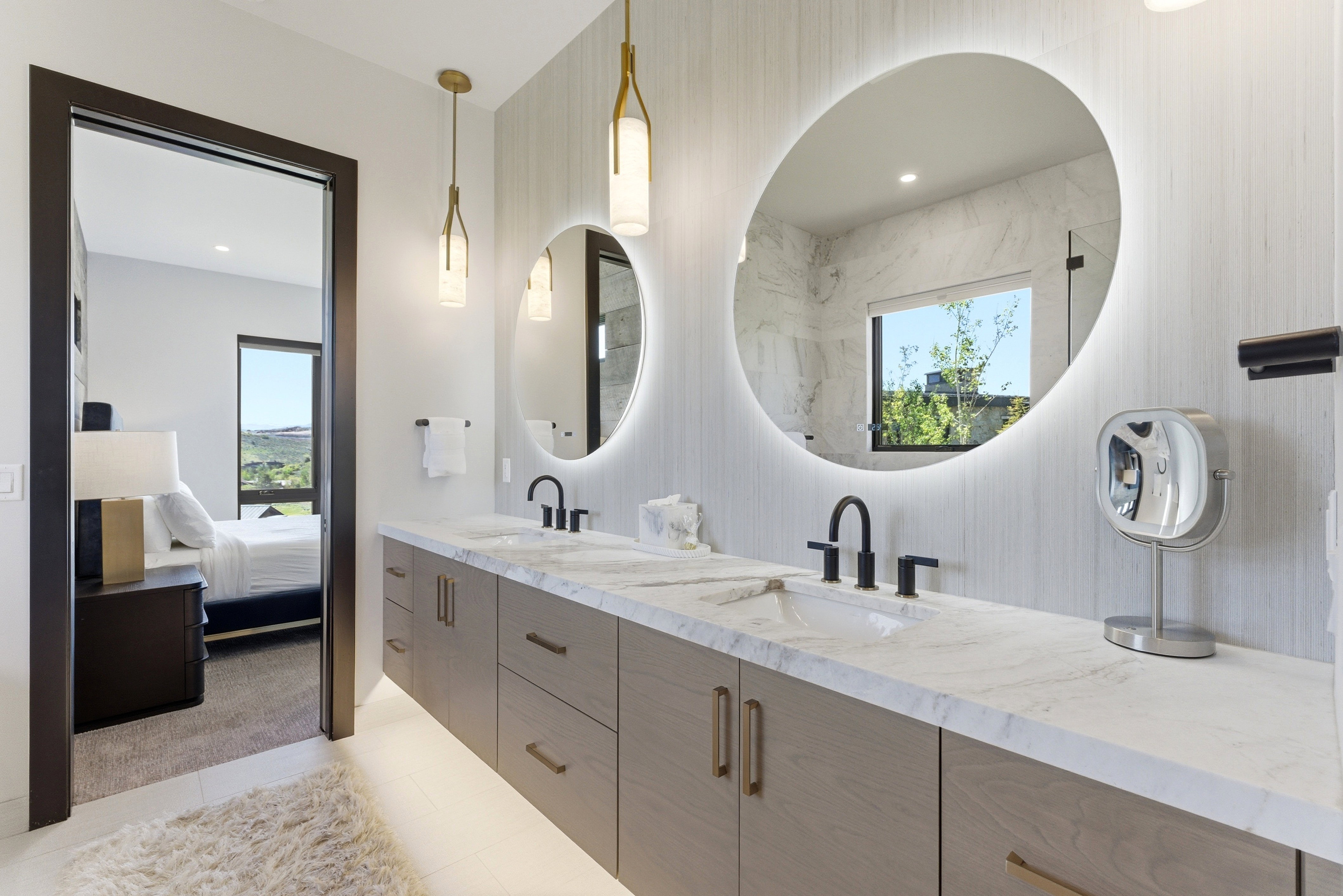 Dual vanity featuring two undermount sinks with matte black fixtures, a light wood-finish cabinetry base with gold-tone hardware, and a light-toned stone countertop