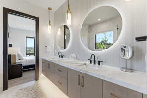 Dual vanity featuring two undermount sinks with matte black fixtures, a light wood-finish cabinetry base with gold-tone hardware, and a light-toned stone countertop