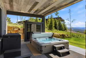 Covered outdoor patio featuring a hot tub with steps, an adjacent storage unit, and a concrete surface