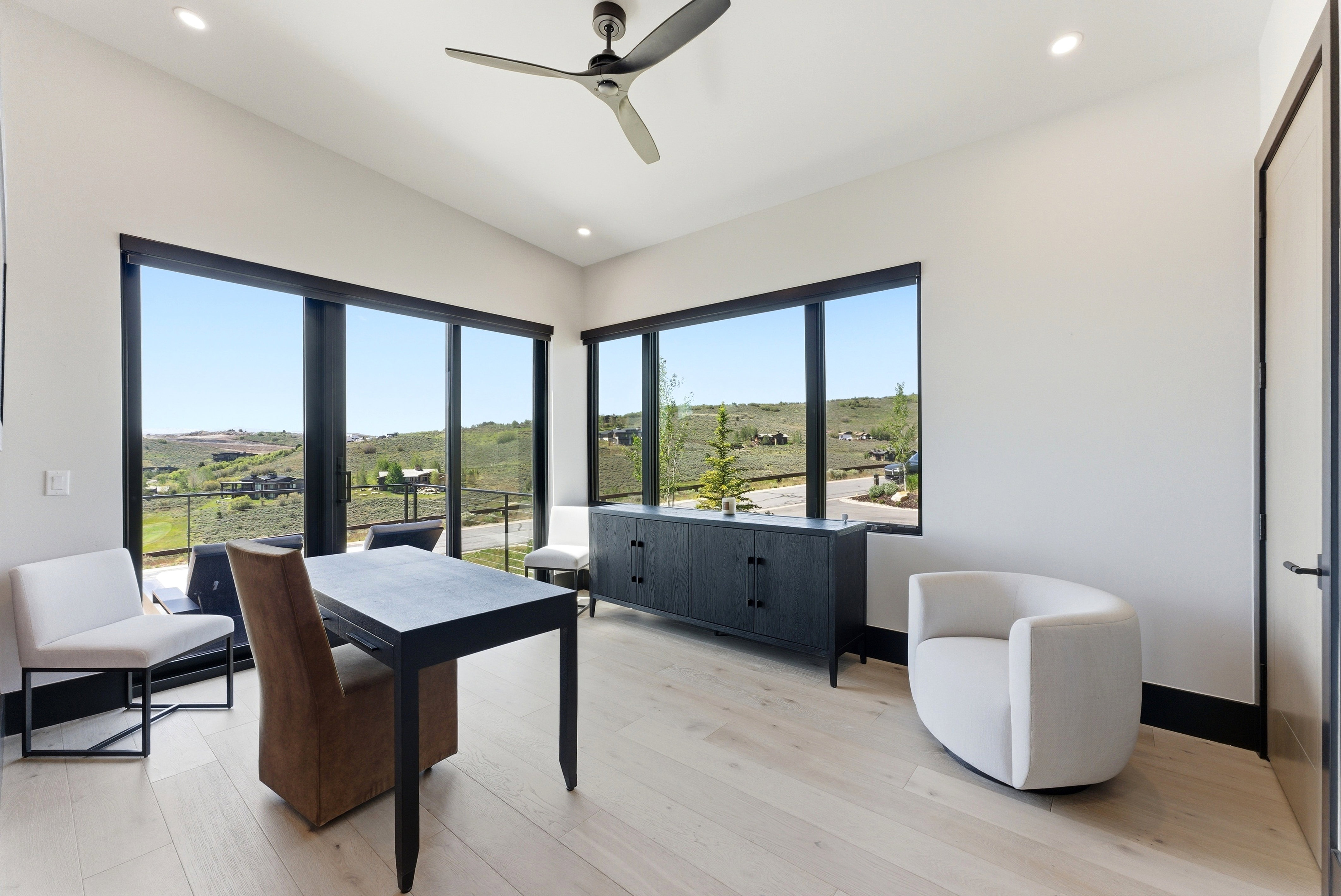 Bright interior space featuring expansive windows, light wood-finish flooring, a contemporary ceiling fan, recessed lighting, and a built-in dark wood console