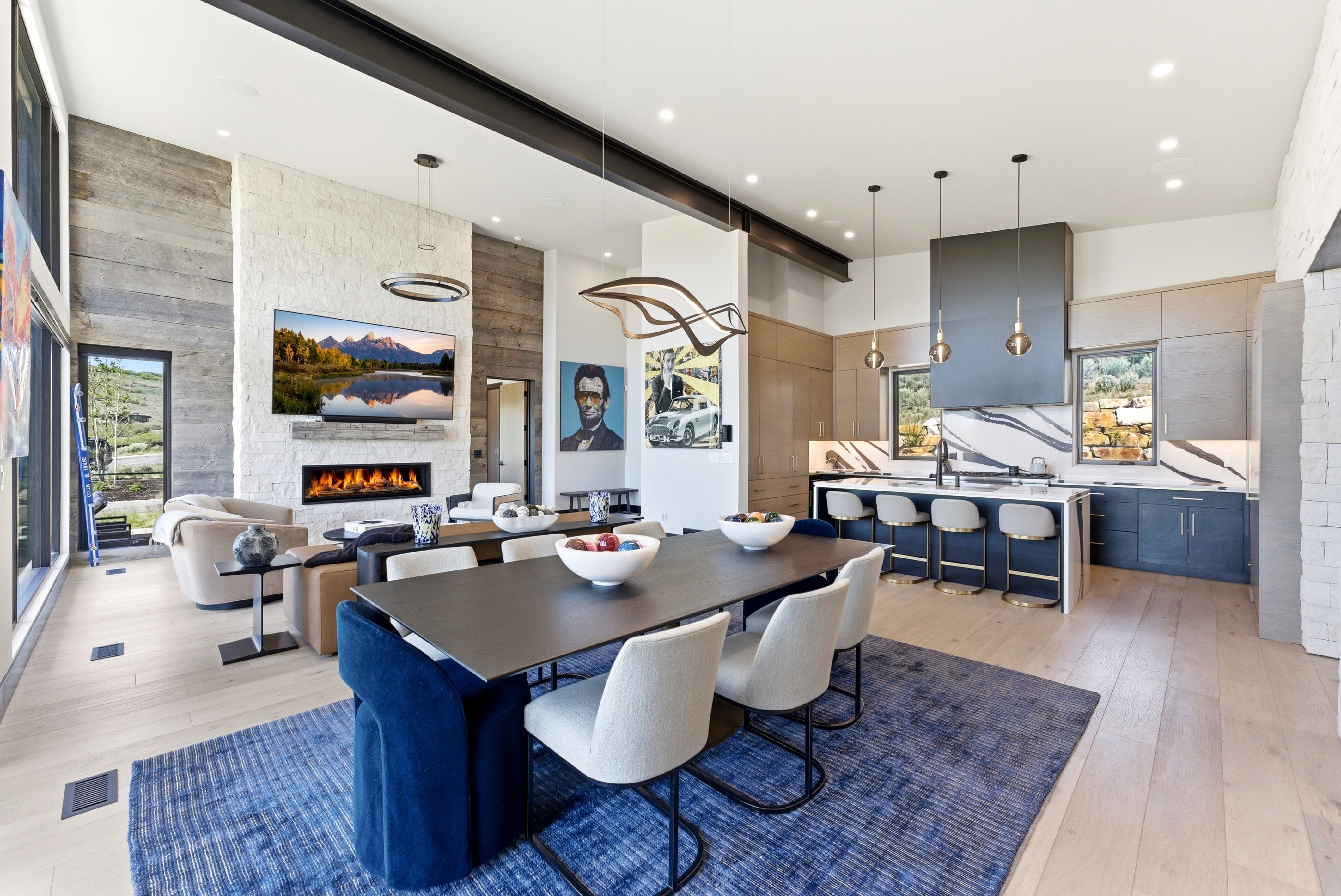Open-concept living space featuring a modern linear fireplace, high ceilings with exposed beams, and light wood-finish flooring