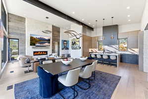 Open-concept living space featuring a modern linear fireplace, high ceilings with exposed beams, and light wood-finish flooring