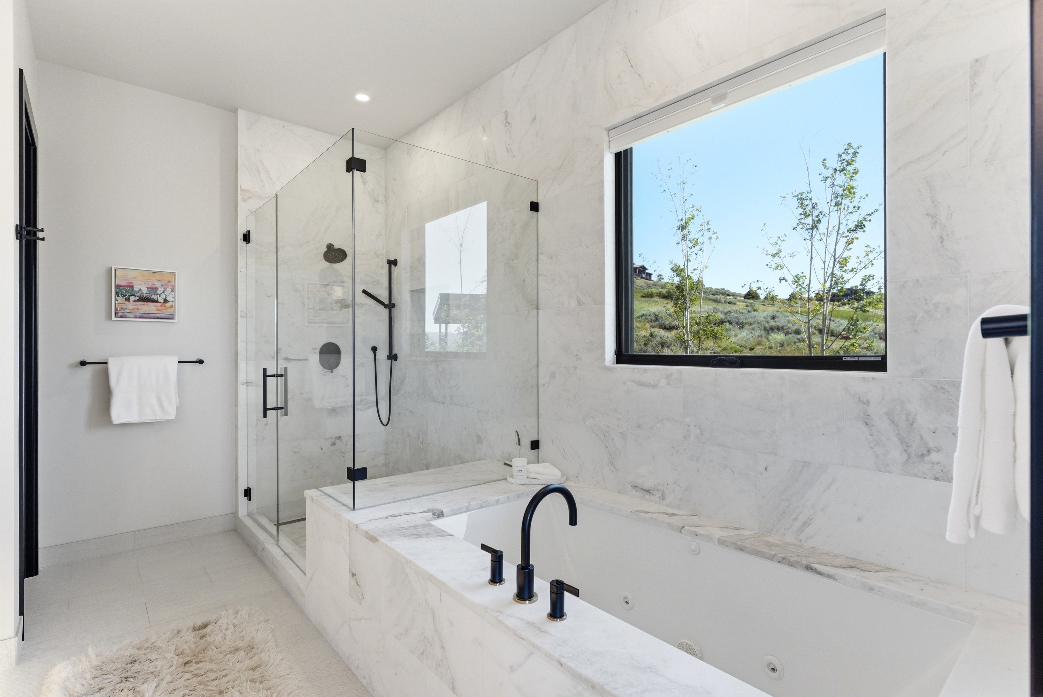 Bathroom featuring a glass-enclosed shower with matte black fixtures, an integrated soaking tub with a matte black faucet, and a large window showcasing a natural landscape