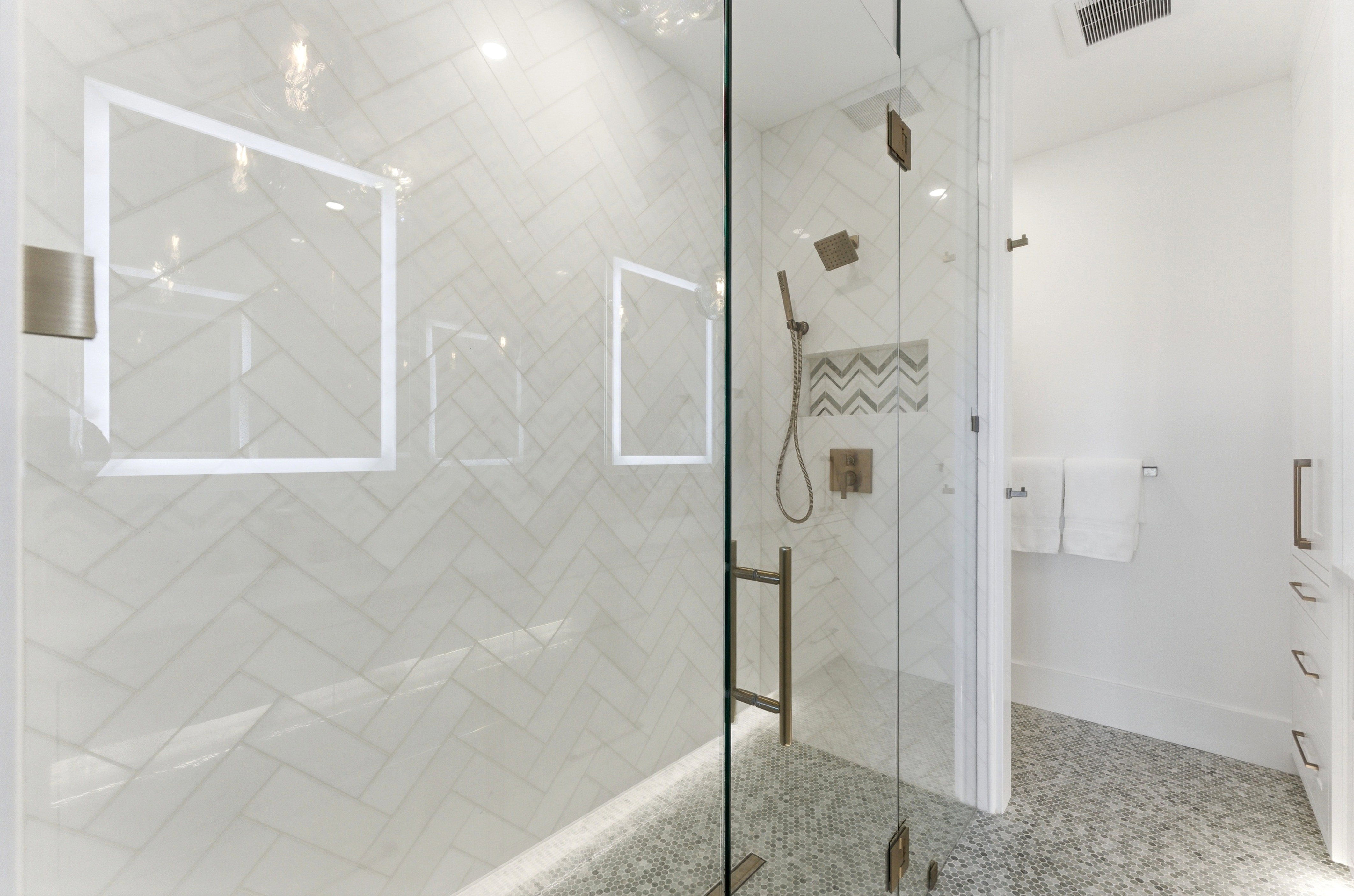 Walk-in shower featuring a frameless glass enclosure and herringbone tile walls