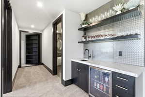 Wet bar featuring a mini-refrigerator, dark cabinetry, and a light-toned countertop