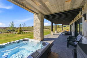 Expansive covered patio featuring a built-in hot tub, concrete flooring, and a wood-finish ceiling