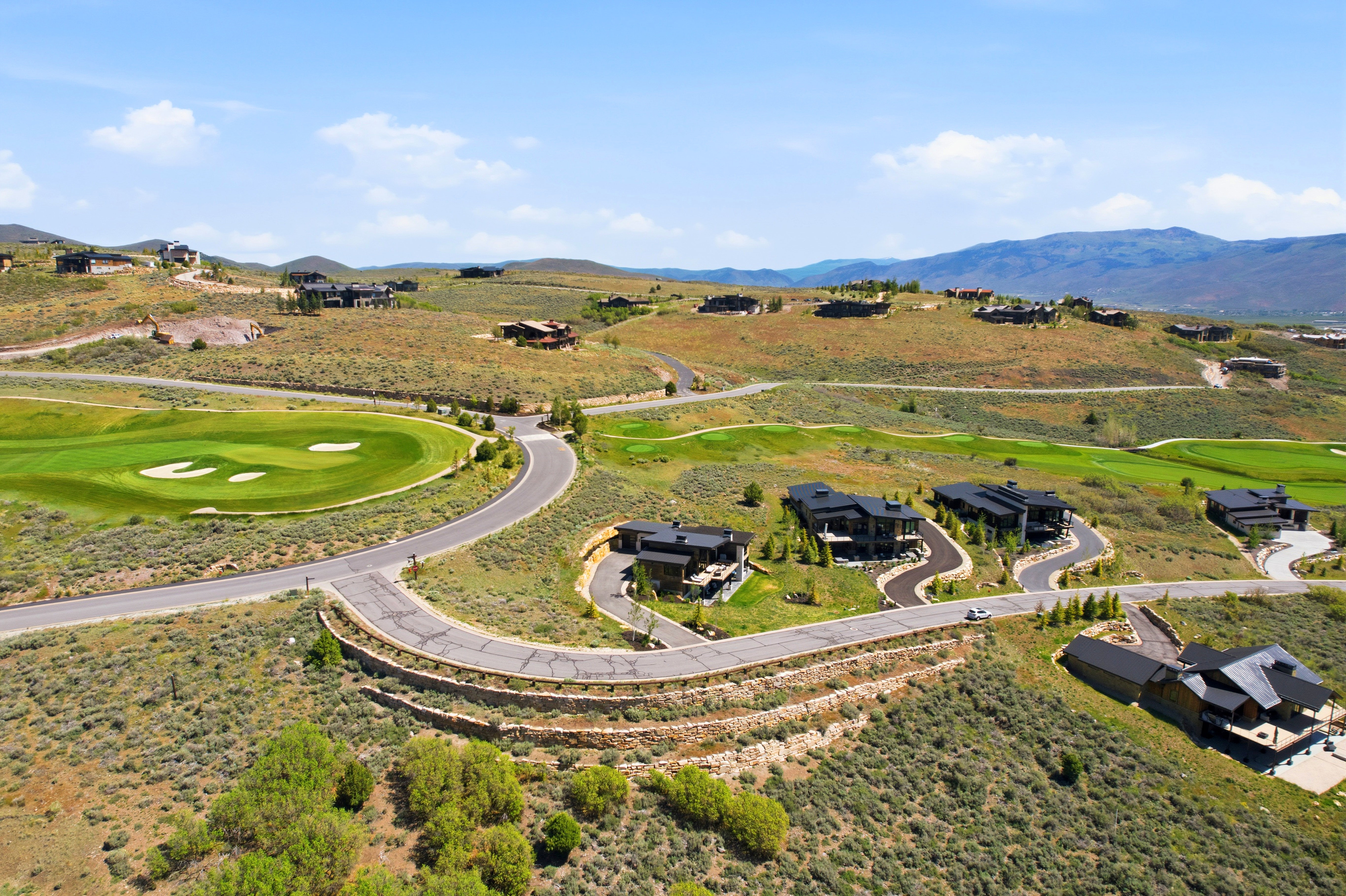 Expansive golf course community featuring winding roads, multiple contemporary residences, and distant mountain ranges