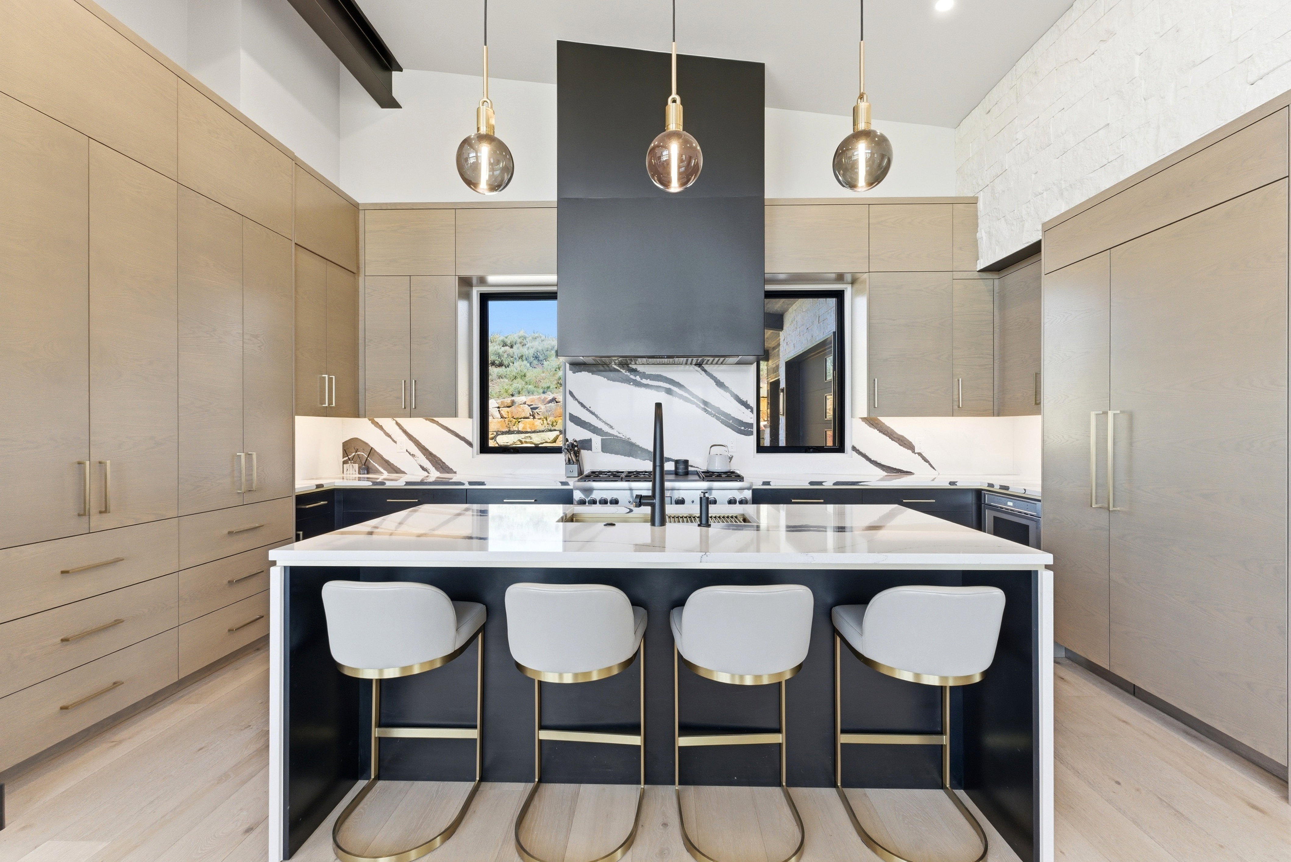 Spacious kitchen featuring a large central island with seating, a professional-grade range, custom light wood-finish cabinetry, integrated refrigerator, and striking patterned slab backsplashes