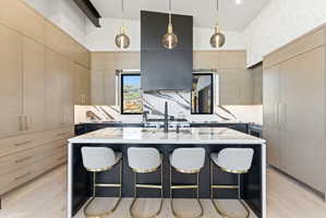 Spacious kitchen featuring a large central island with seating, a professional-grade range, custom light wood-finish cabinetry, integrated refrigerator, and striking patterned slab backsplashes