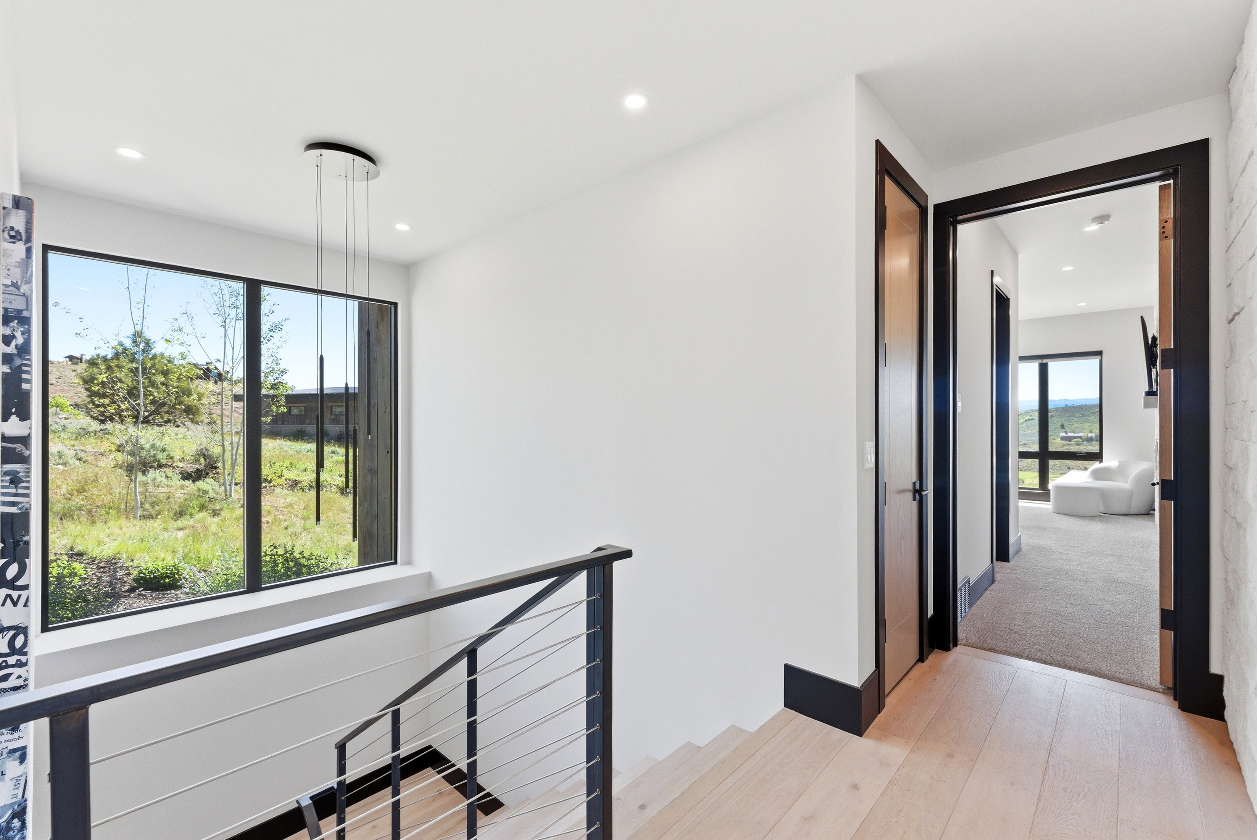 Upper landing with wood-finish flooring, a contemporary cable railing system, and a large picture window offering exterior scenery