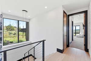Upper landing with wood-finish flooring, a contemporary cable railing system, and a large picture window offering exterior scenery