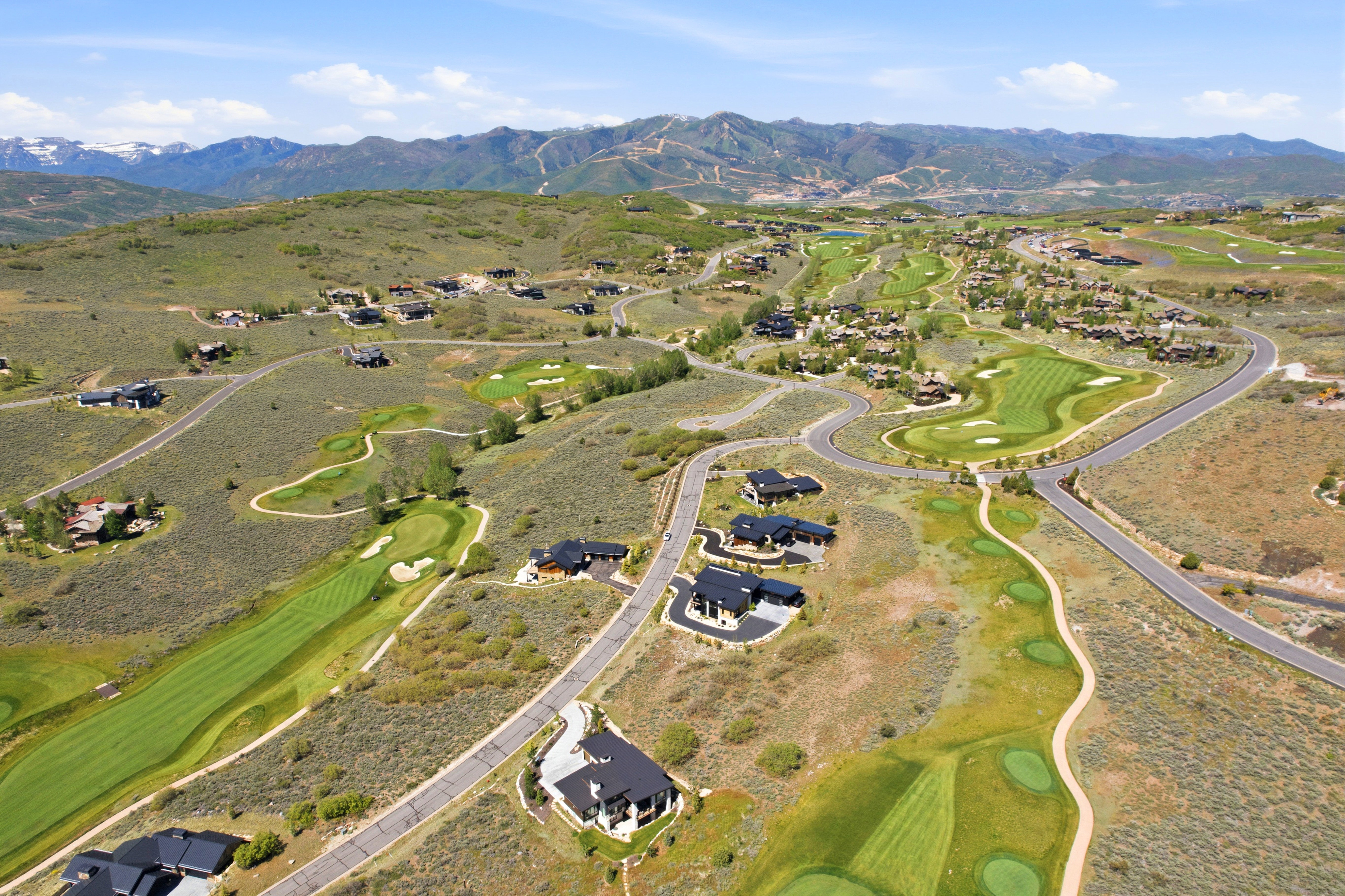 Expansive mountain landscape featuring a golf course, residential properties, paved roadways, and distant snow-capped mountains