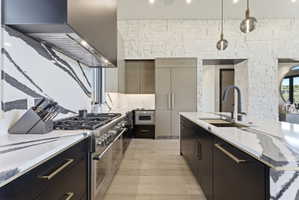 Gourmet kitchen featuring a professional-grade gas range, custom black cabinetry with gold hardware, a large kitchen island with integrated sink, and an accent wall of stacked stone veneer