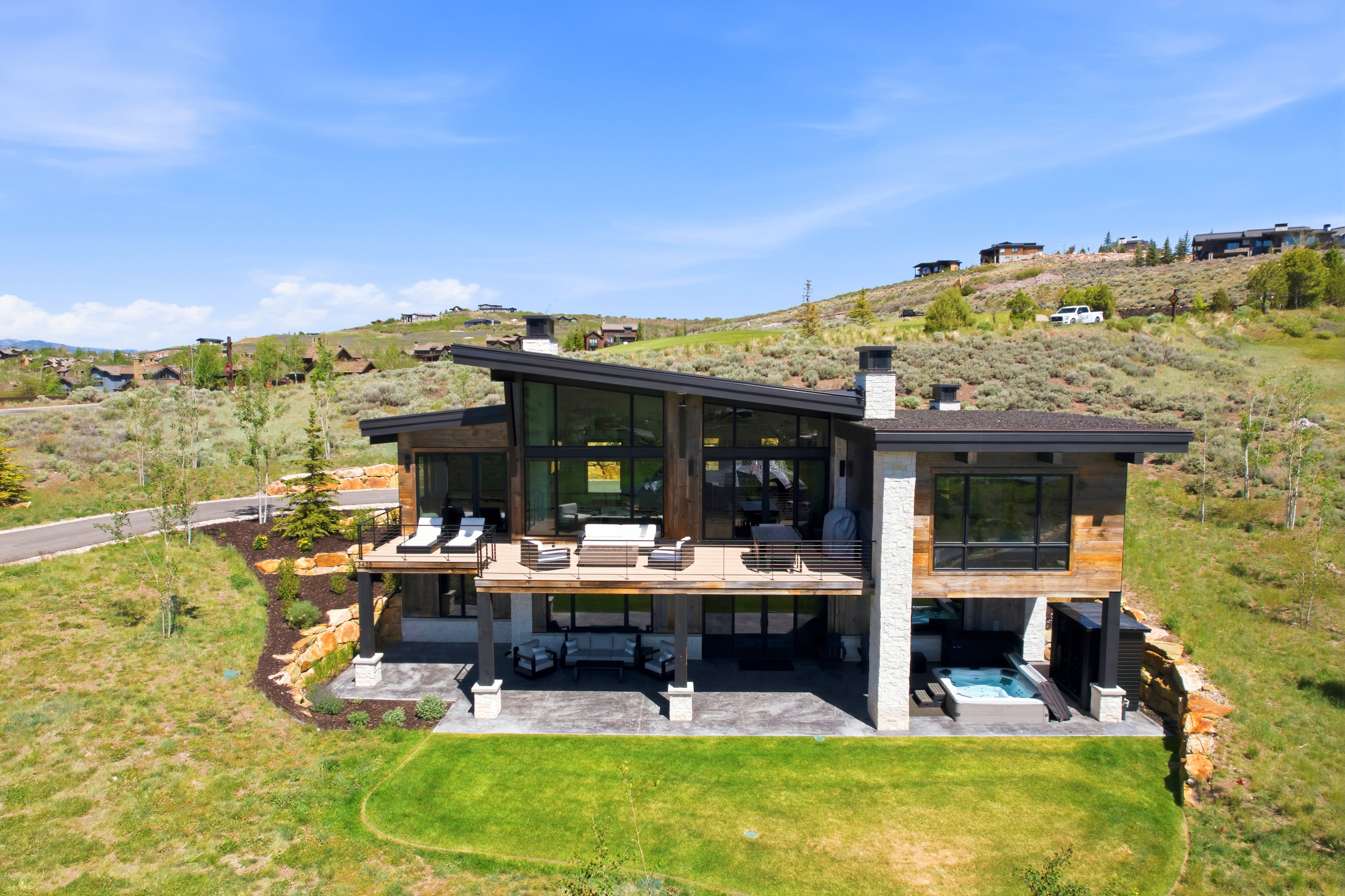 Multi-level modern residence featuring extensive glazing, a prominent upper deck, and a lower patio with an integrated spa