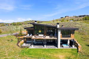 Multi-level modern residence featuring extensive glazing, a prominent upper deck, and a lower patio with an integrated spa