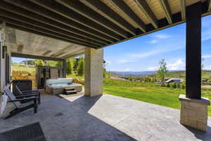 Expansive outdoor patio featuring a hot tub, stamped concrete flooring, and a stone-clad column