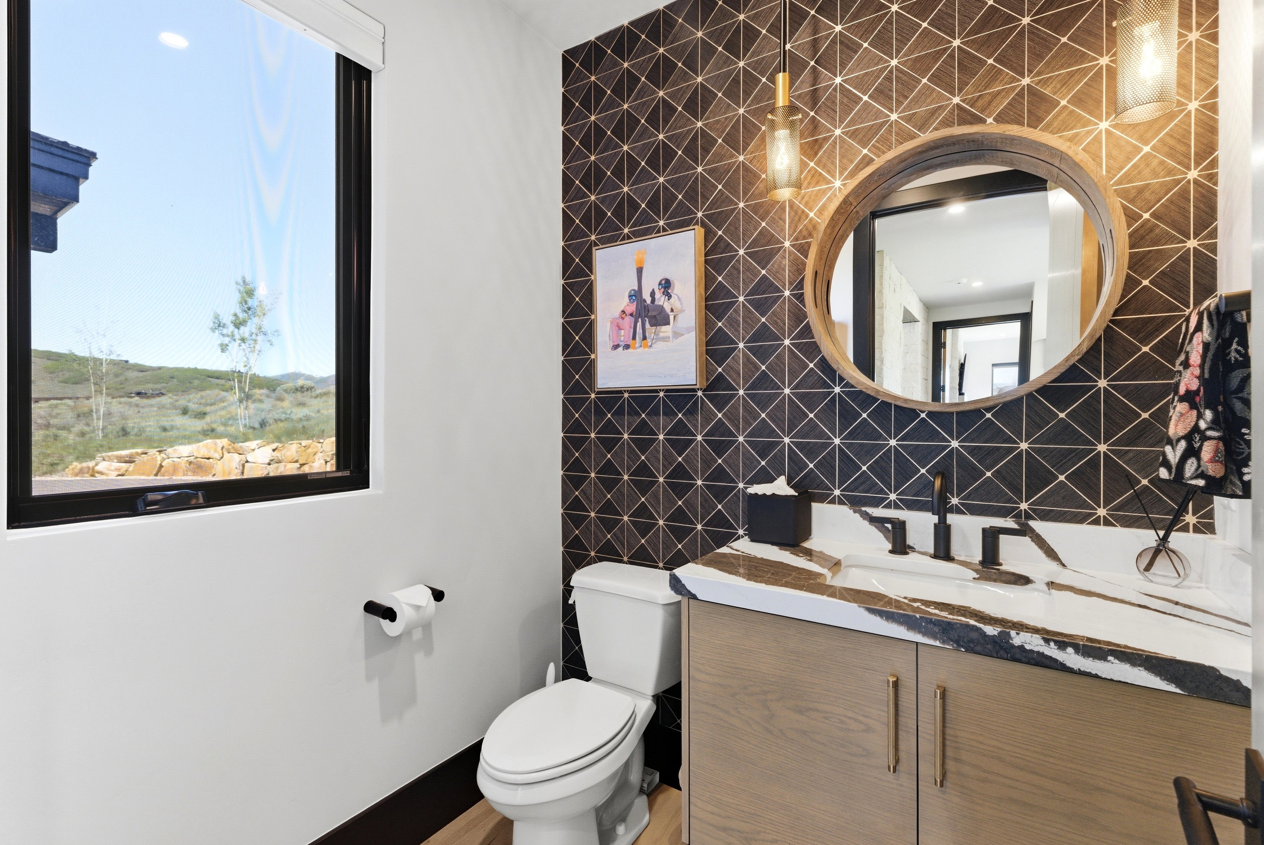Modern powder room featuring a patterned accent wall, a natural wood-finish vanity with gold hardware, and a unique countertop