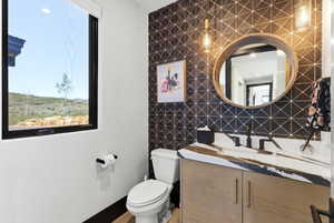 Modern powder room featuring a patterned accent wall, a natural wood-finish vanity with gold hardware, and a unique countertop