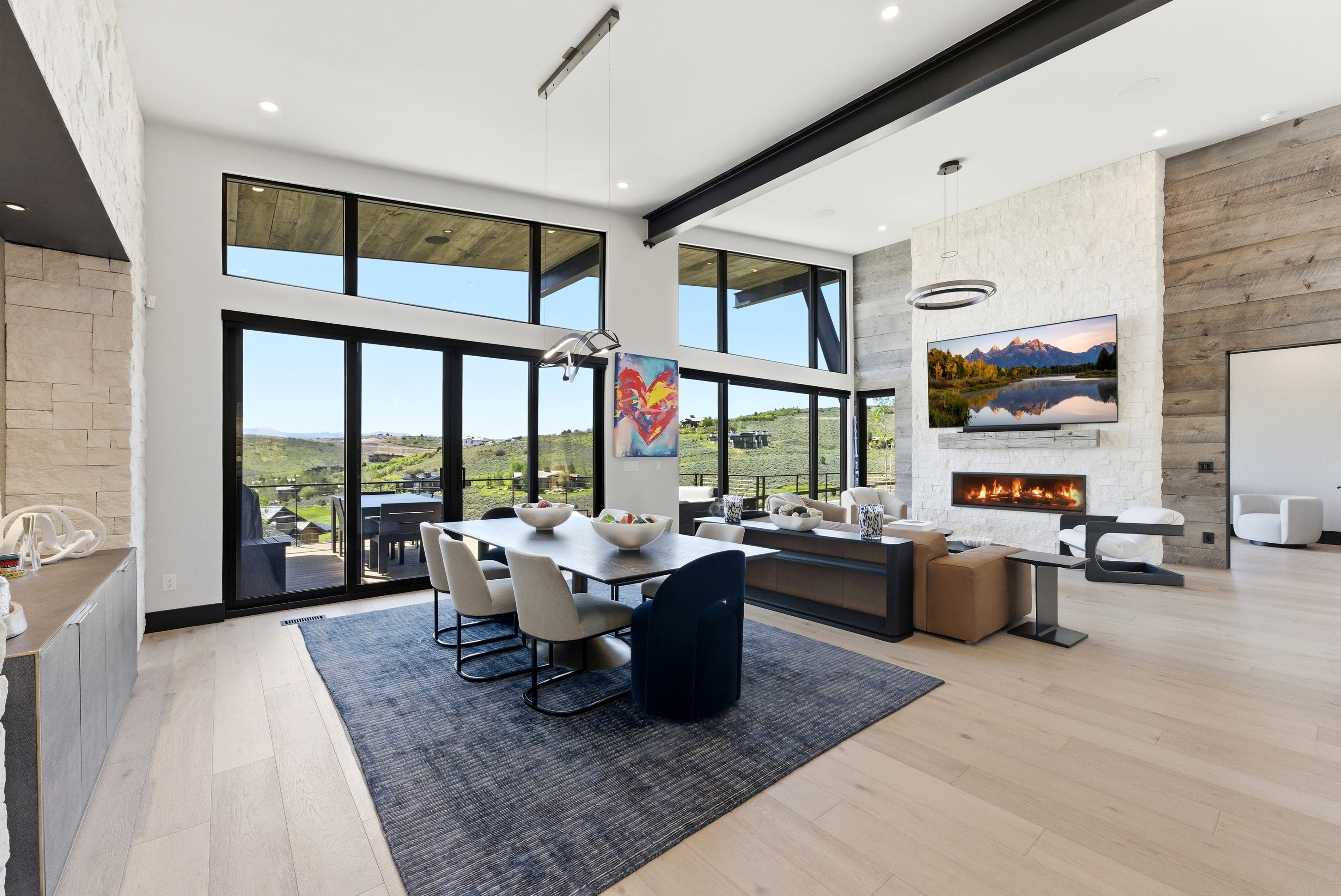 Expansive open-concept room featuring wide plank wood-finish flooring, a contemporary linear fireplace with a stone surround, and floor-to-ceiling windows with a transom