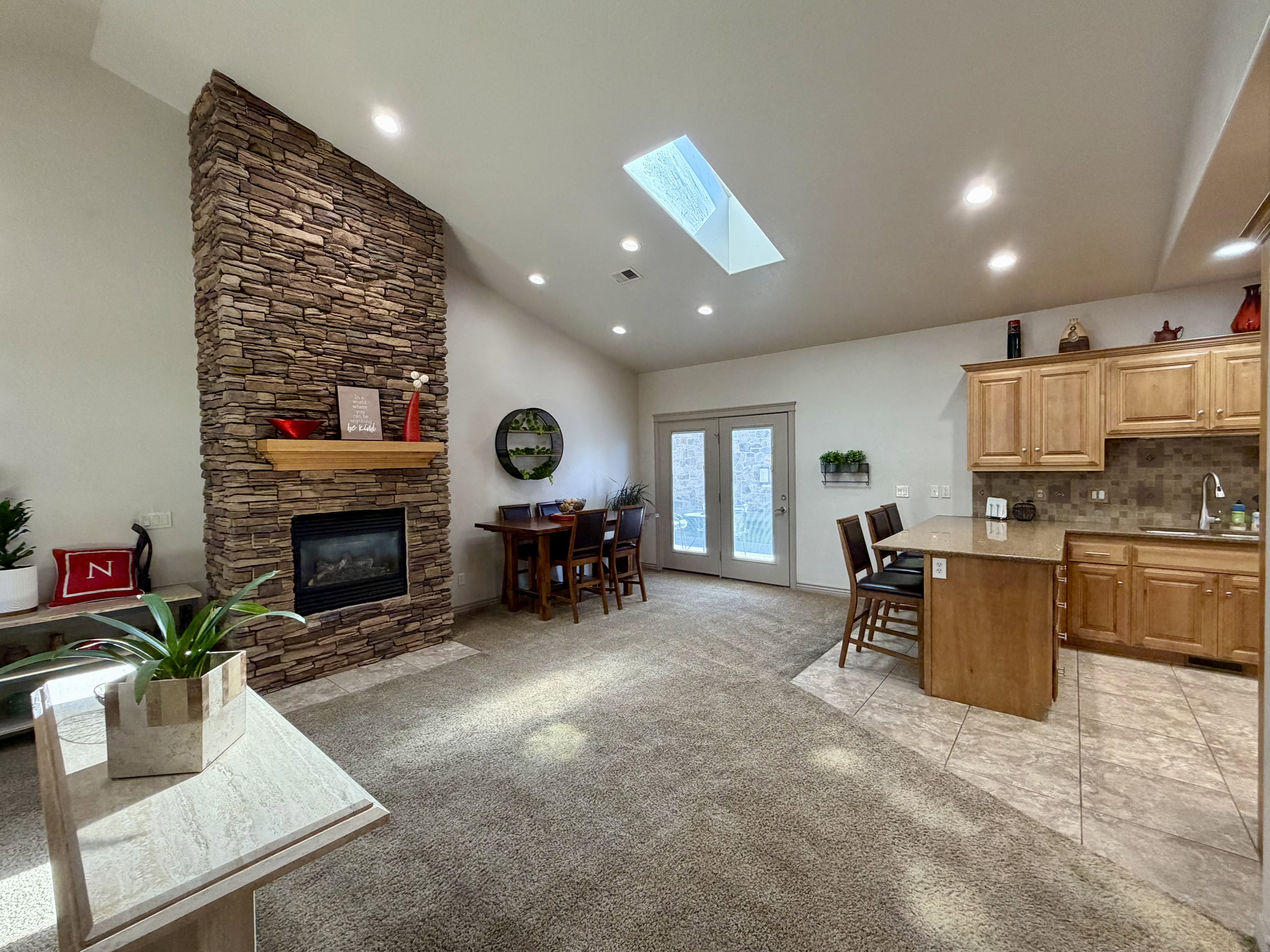 Open-concept living area featuring a stone-clad fireplace with a wood mantel, vaulted ceilings, and a skylight with sliding patio extends the living area outdoors