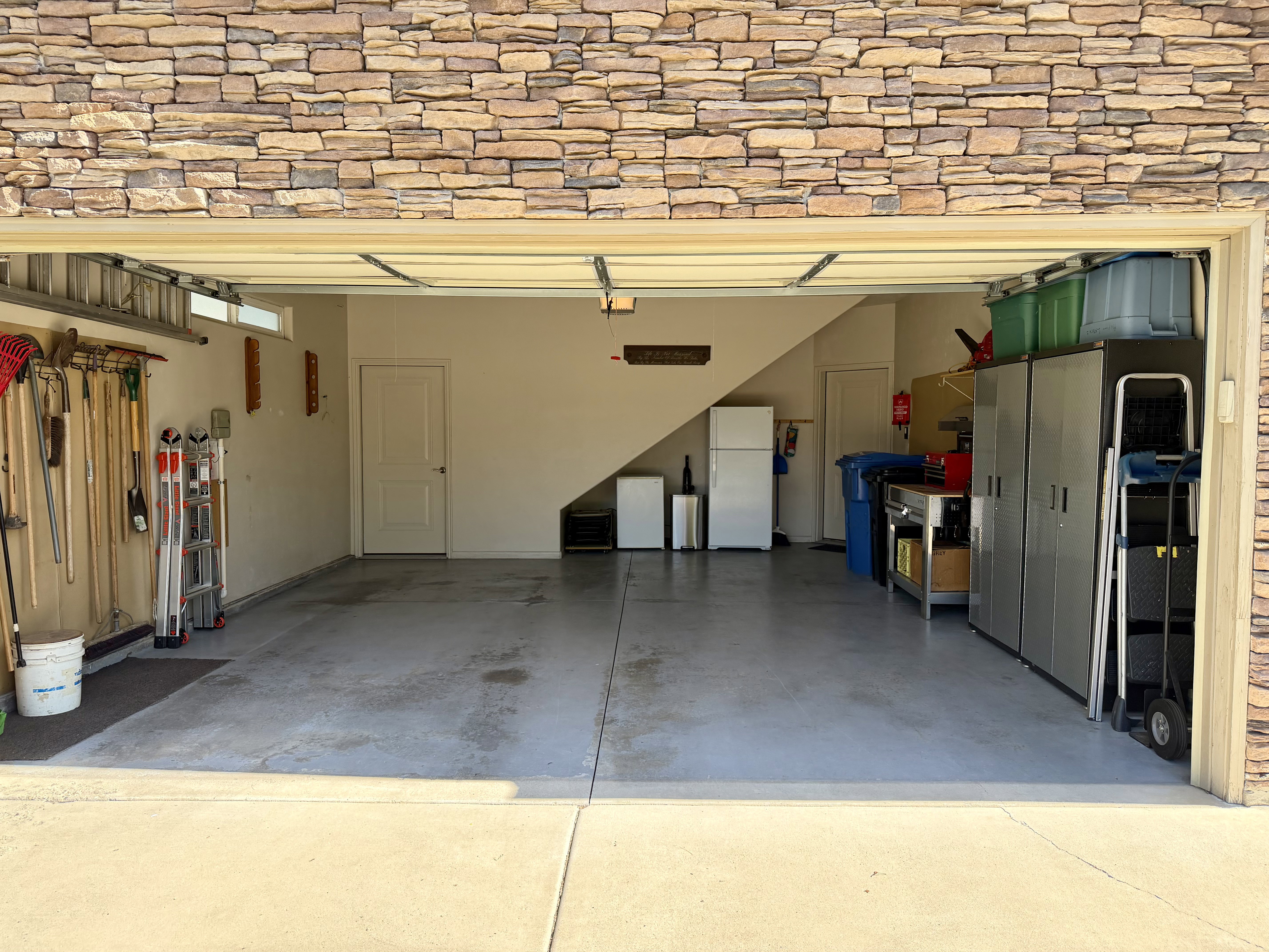 Spacious garage with a stone veneer exterior, an interior access door, a built-in window, access to attic storage, and ample ceiling height