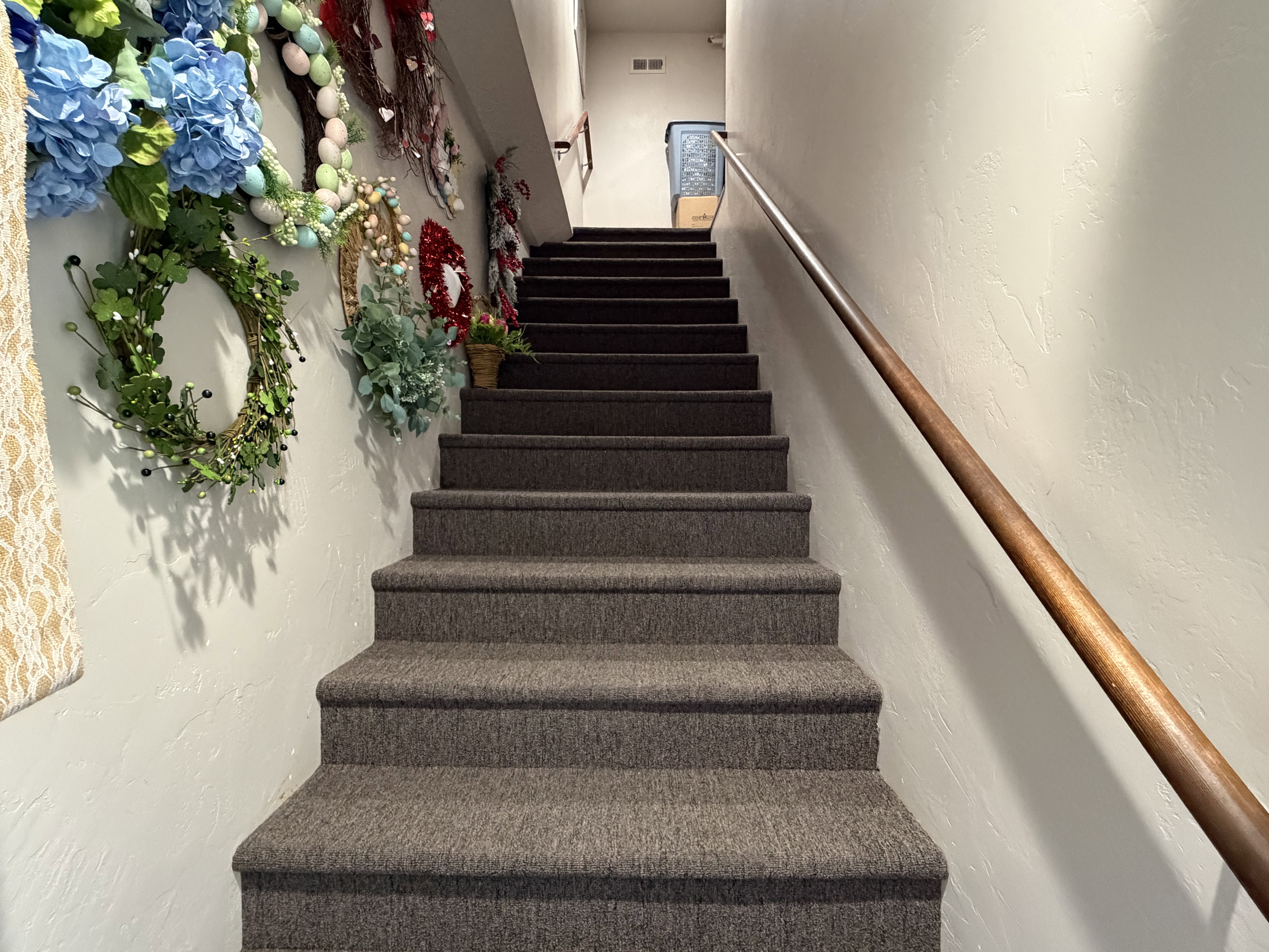 Conveniently wide carpeted staircase with a wood handrail leading to attic access