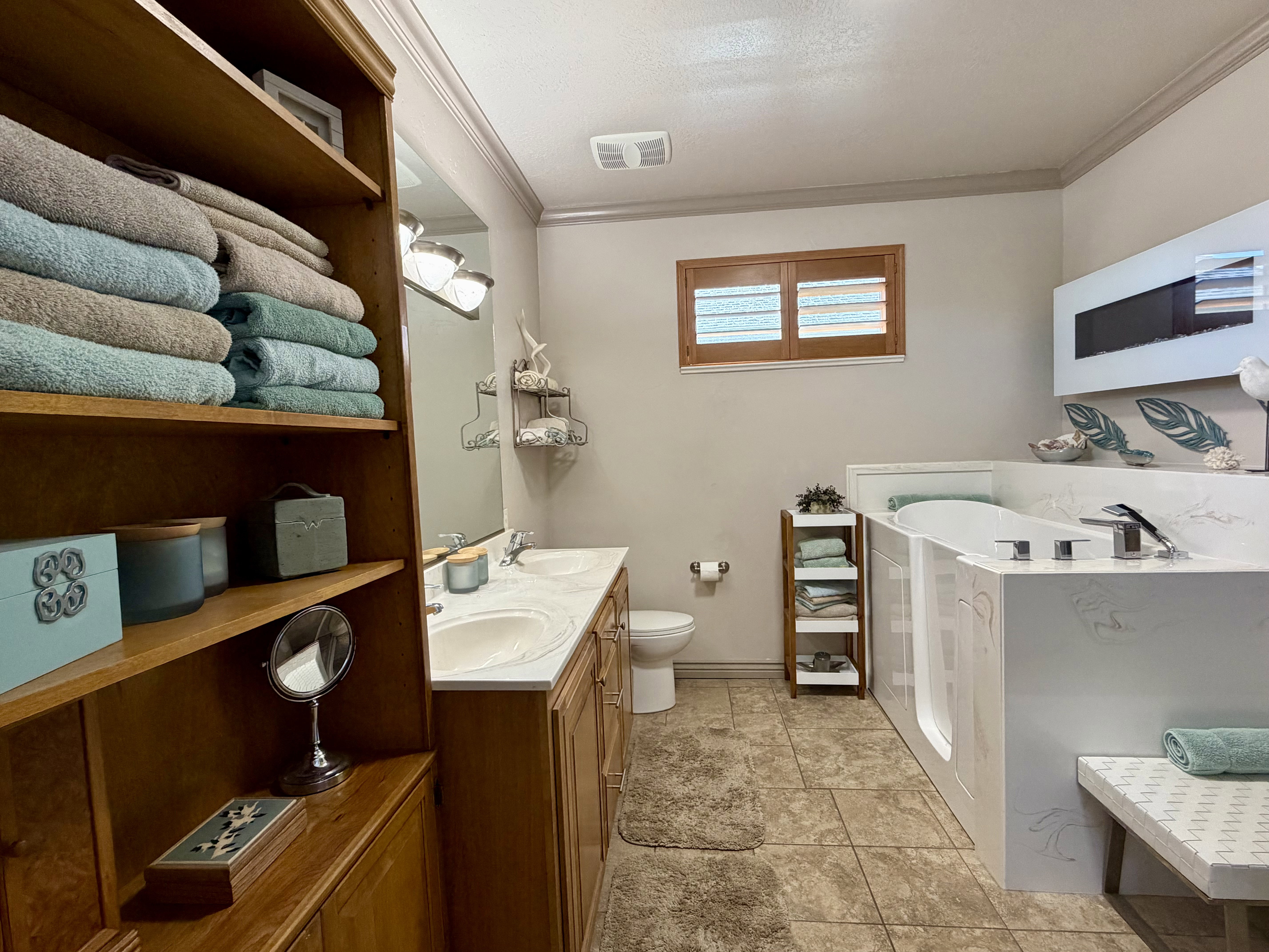 Master Bathroom featuring a walk-in tub with build in fireplace, integrated bench seating, dual vanity with under-mount sinks and light-toned countertops, wood-finish cabinetry, and tiled flooring