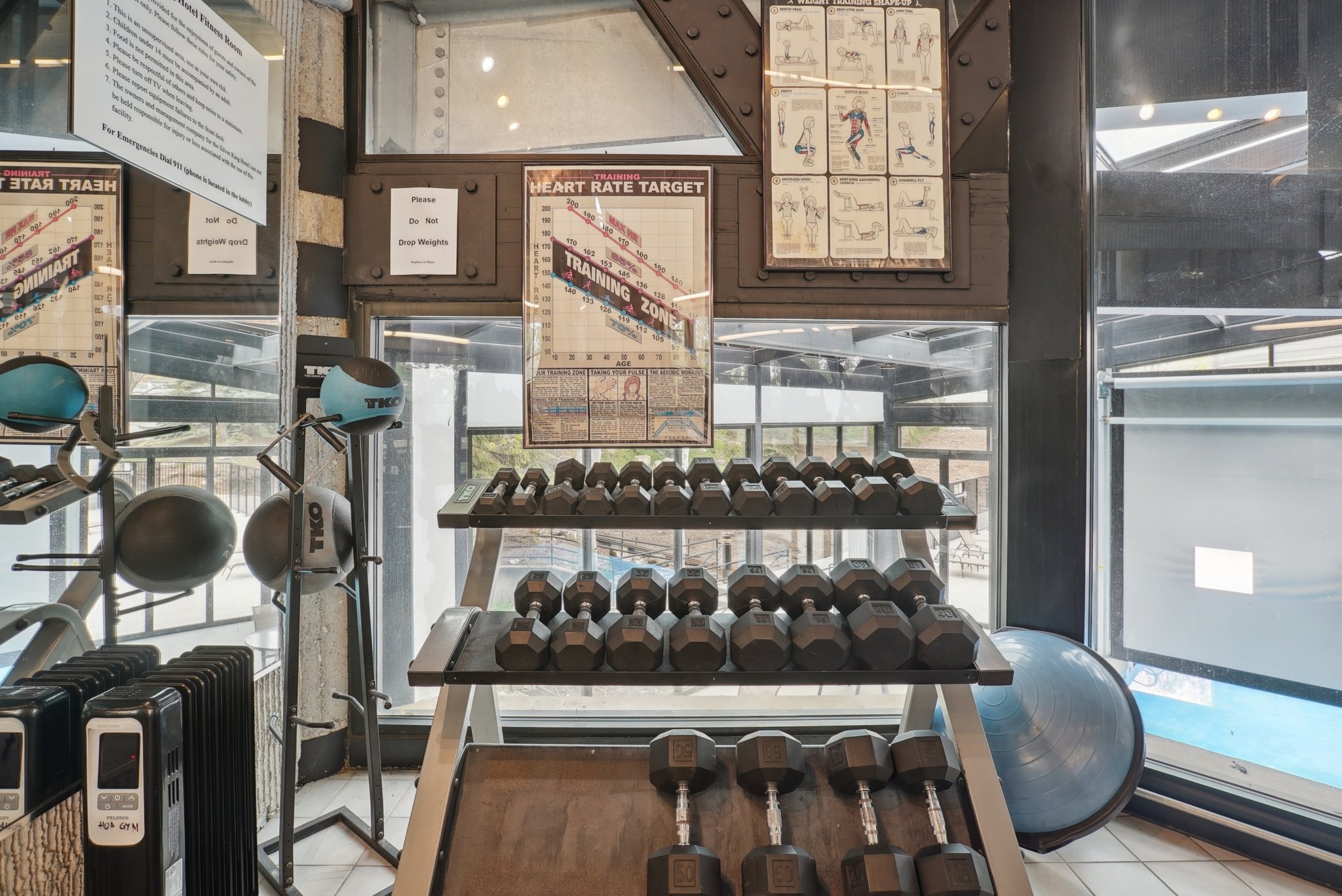 Dedicated fitness area featuring a comprehensive dumbbell rack, ample natural light, and structural beams