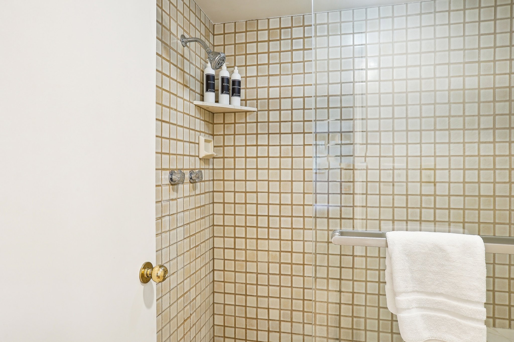 Shower enclosure with square tile surround, clear glass panel, wall-mounted shower head, and chrome fixtures