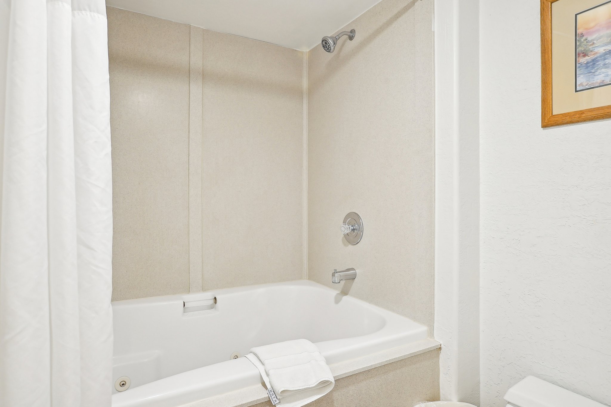 White shower curtain enclosing a built-in bathtub with integrated jets and chrome fixtures