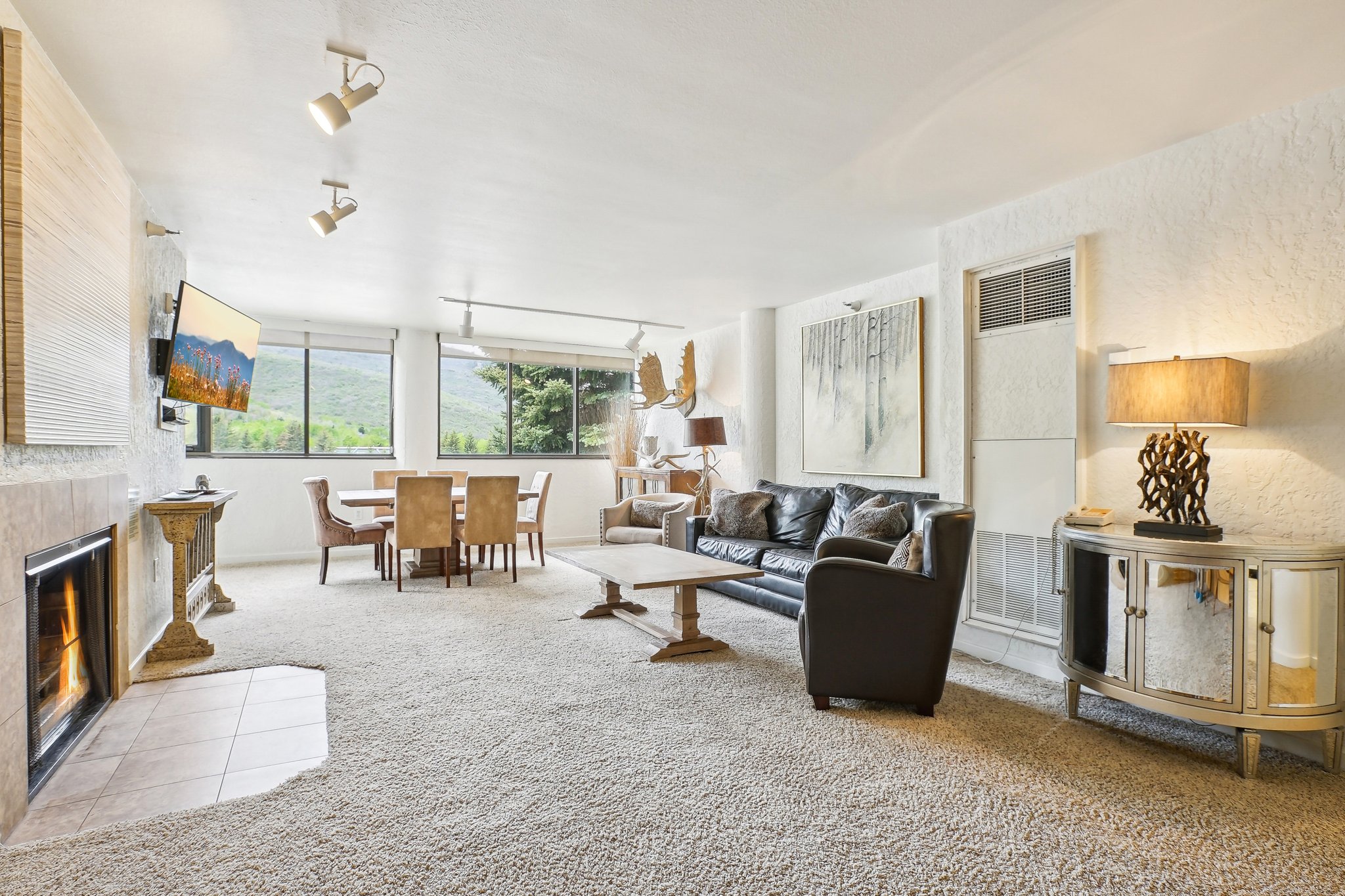 Open-concept living area featuring a stone-clad fireplace with a tiled hearth, track lighting, and expansive windows