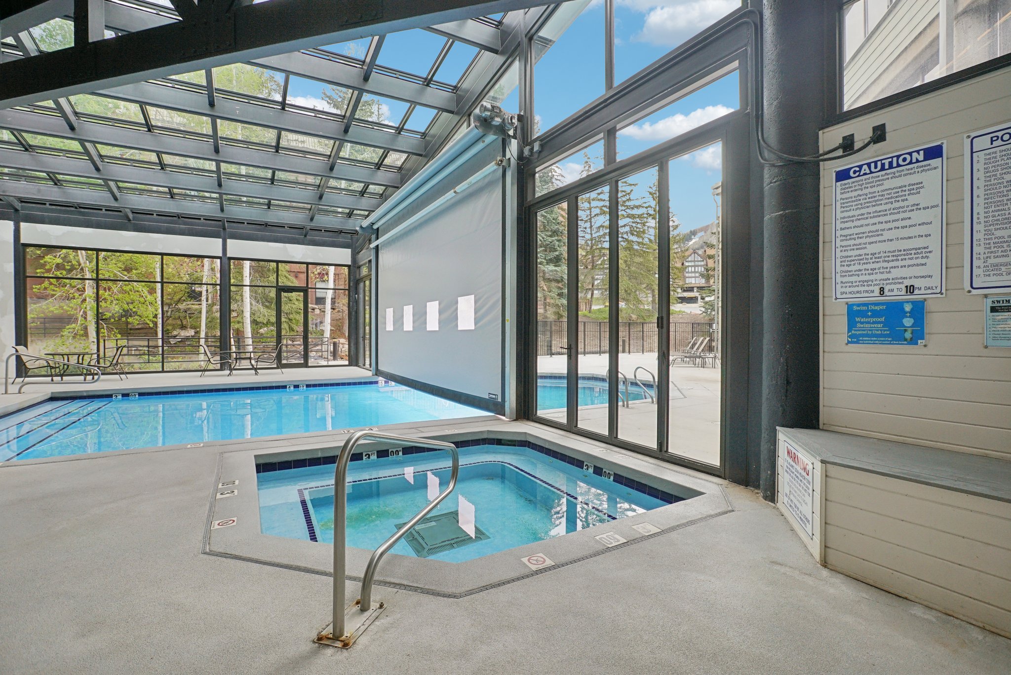 Indoor swimming pool featuring a connected hot tub, a glass ceiling, and floor-to-ceiling windows