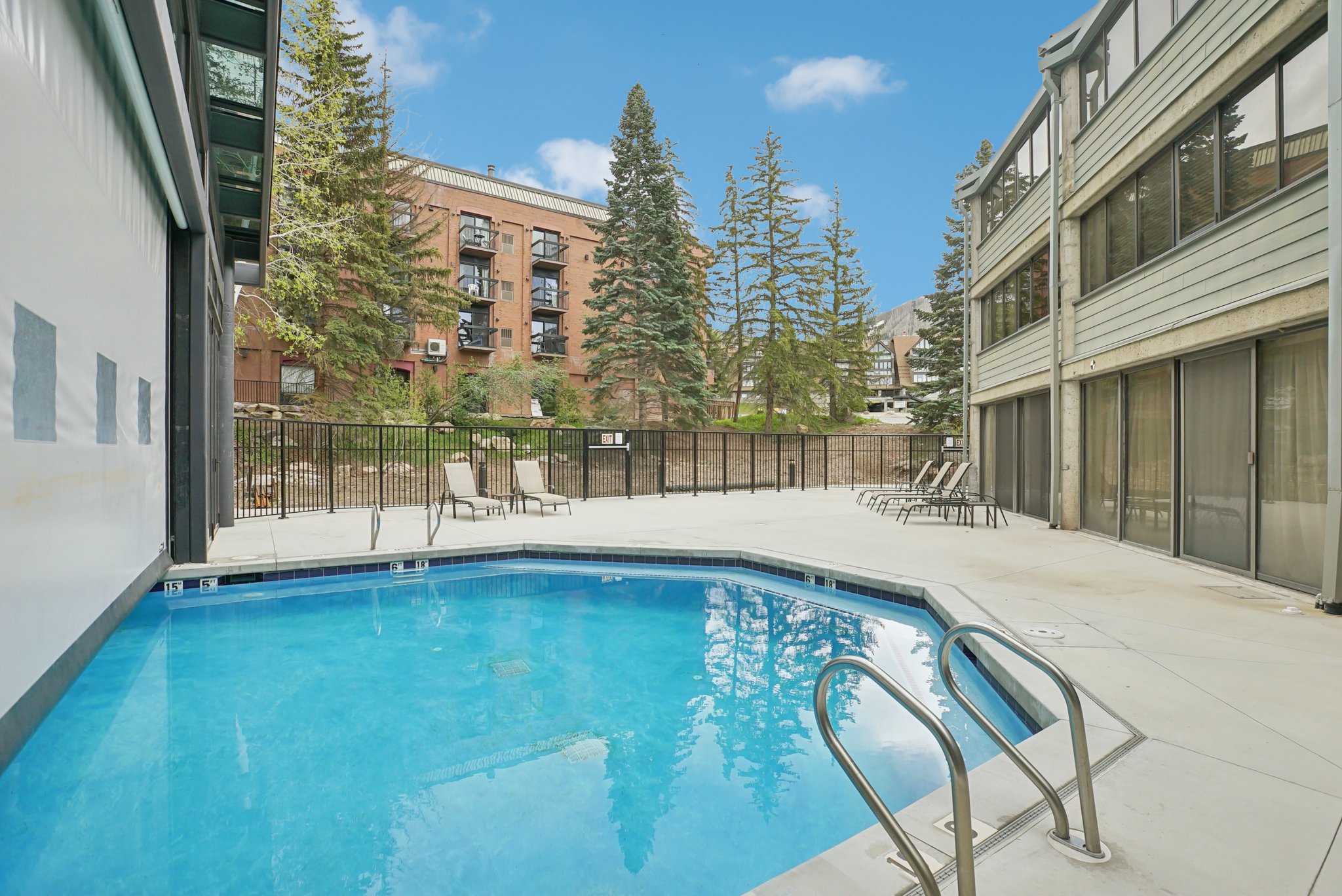 Outdoor swimming pool with concrete decking, surrounded by a black metal fence