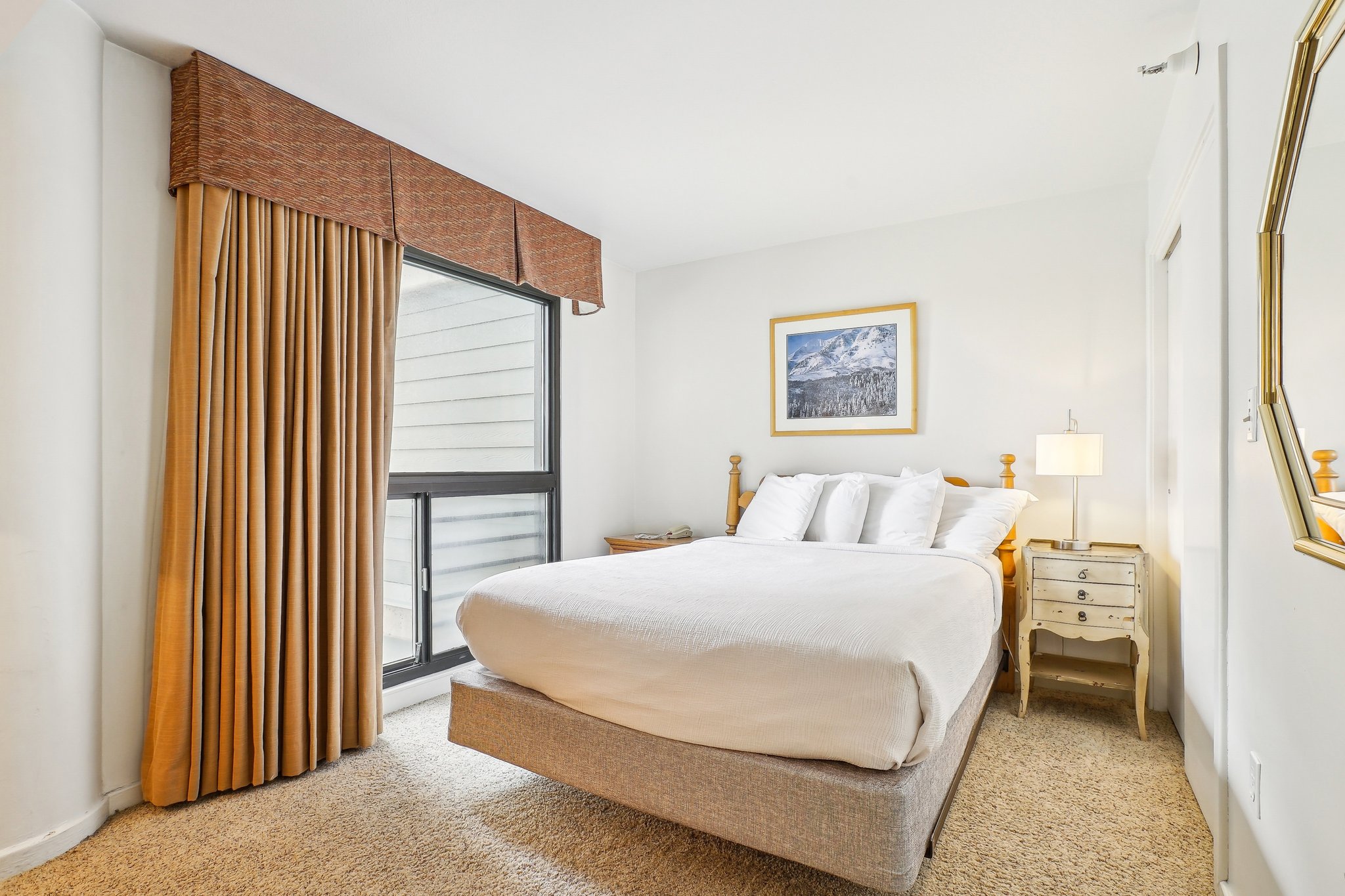 Bedroom featuring a neutral carpet, large picture window with privacy blinds, and a window valance