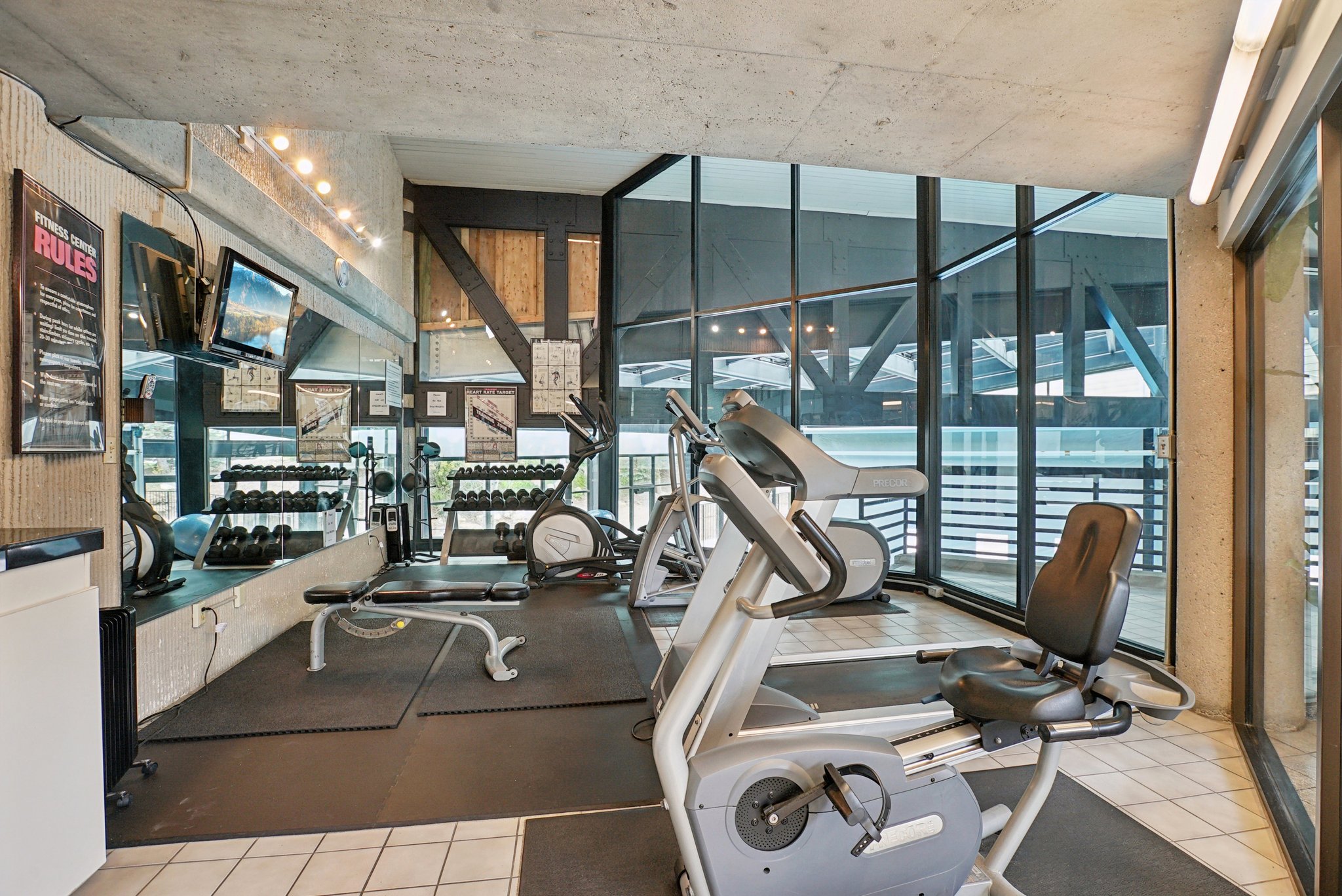 Fitness area featuring a mirrored wall, integrated television displays, and large-pane windows