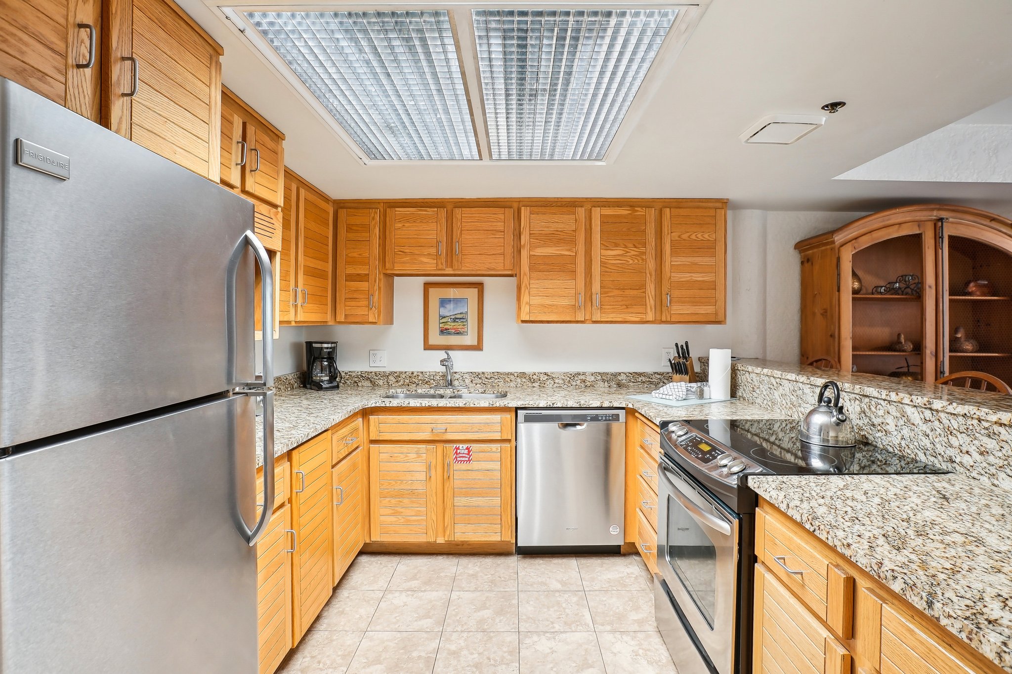 U-shaped kitchen featuring light wood cabinetry, stone countertops, stainless steel appliances, and a tiled floor