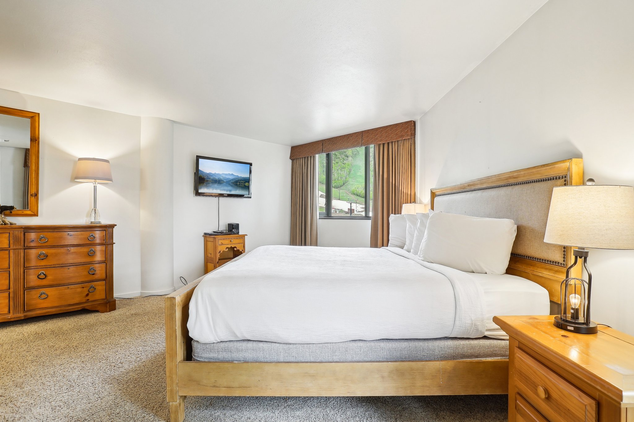Bedroom featuring a light-toned carpet, a window with drapery, and a mounted flat-screen television
