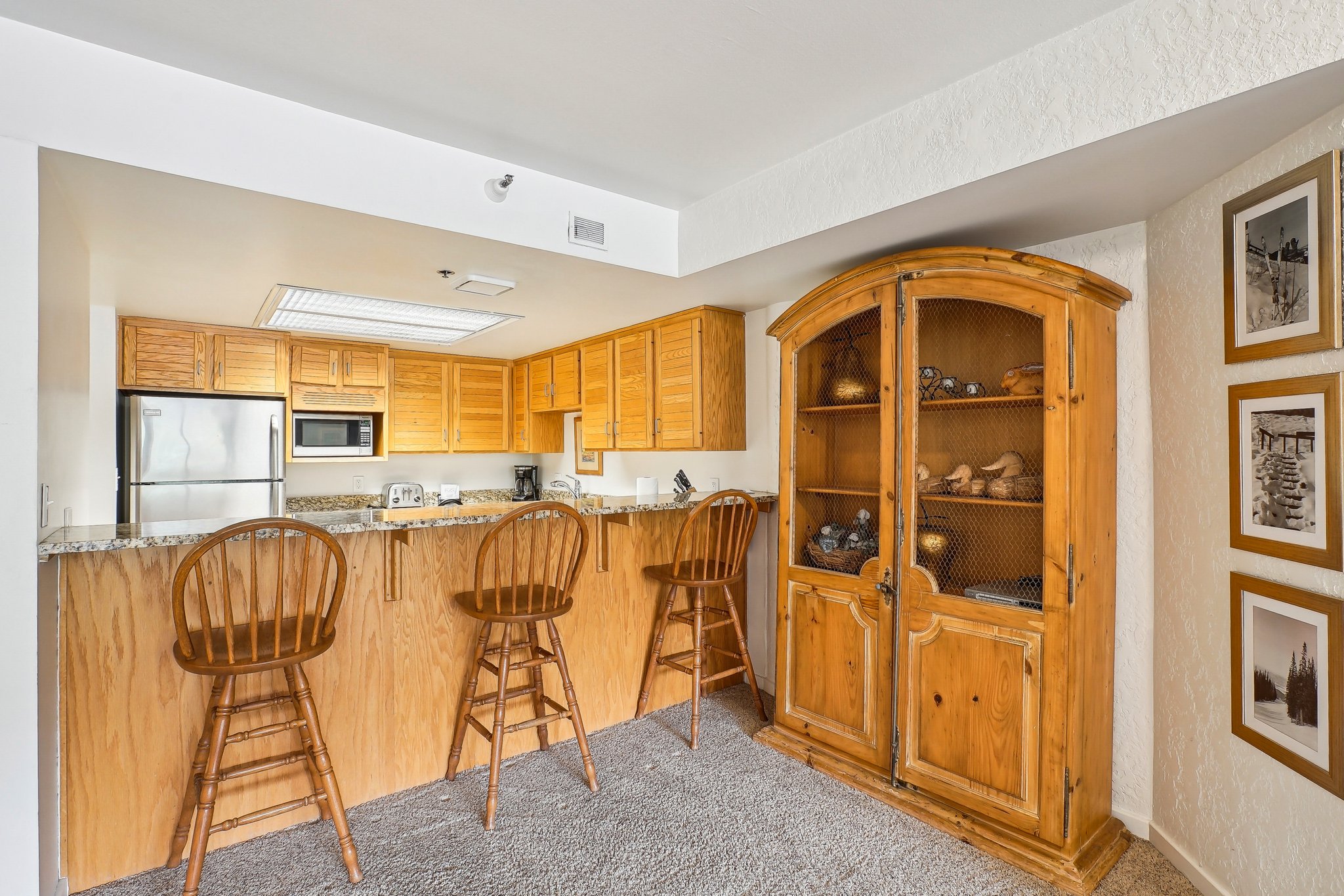 Kitchen area featuring wood-finish cabinetry, granite-style countertops, stainless steel refrigerator, and a built-in microwave