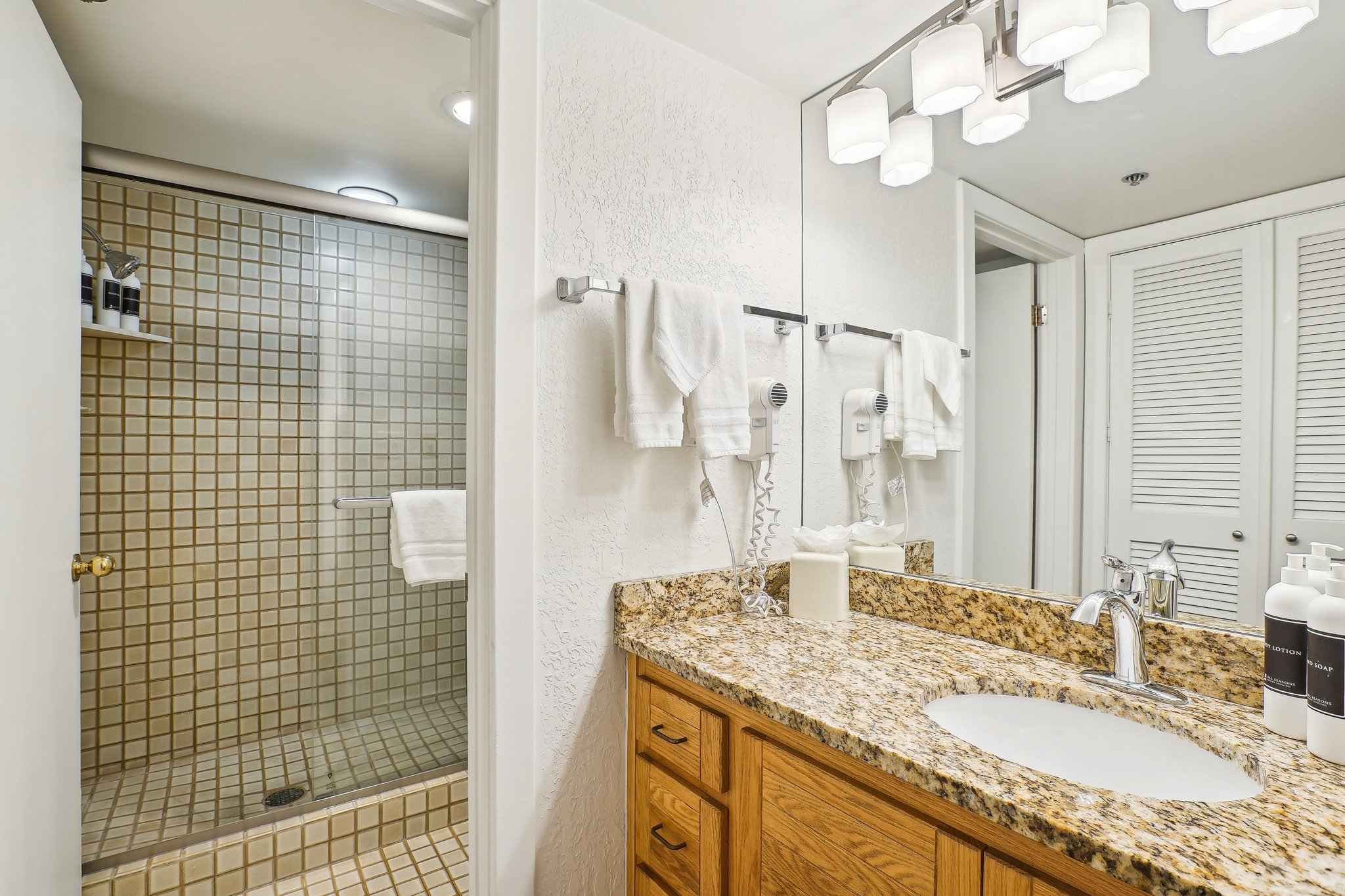 Bathroom featuring a glass-enclosed shower with square tile surround, a single vanity with stone countertop, and wood-finish cabinetry