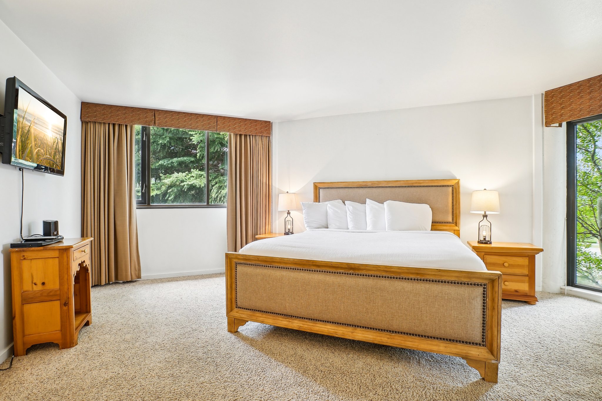 Carpeted bedroom featuring white walls, a large window with tan drapes, and an additional window with a patterned valance