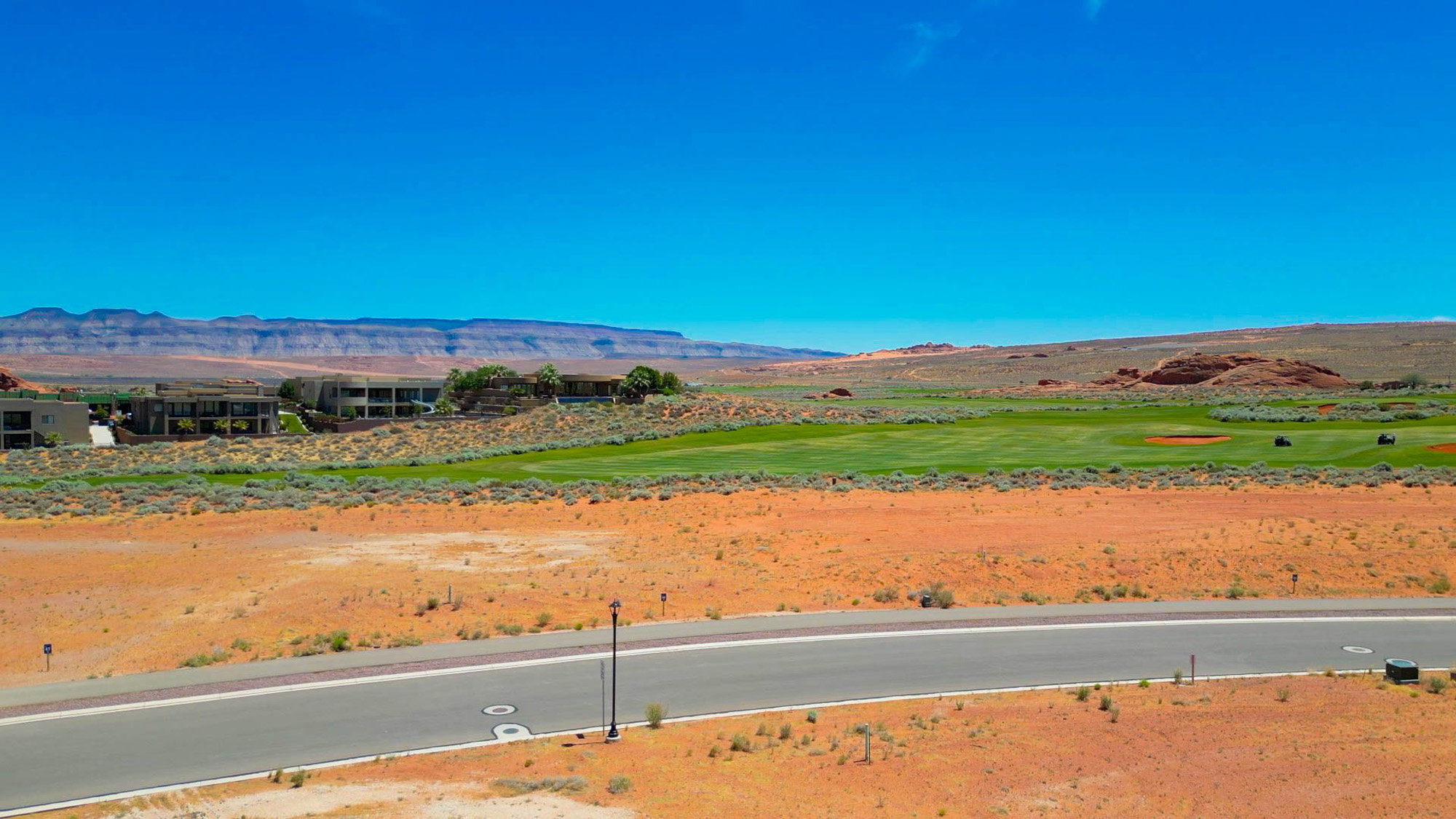 Expansive desert landscape featuring a paved roadway, arid foliage, and distant mountain ranges