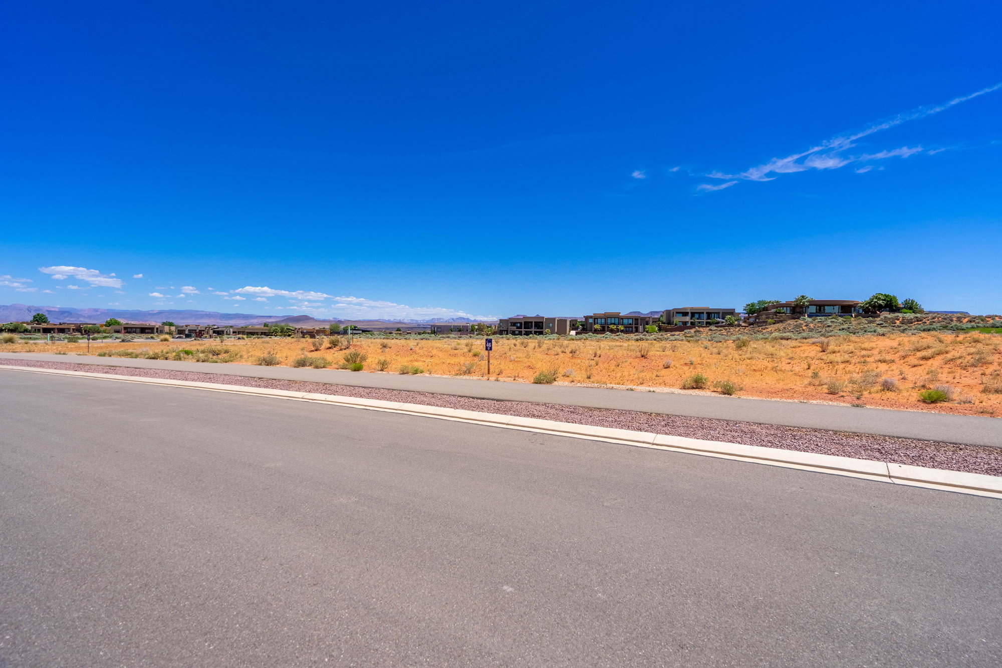 Expansive undeveloped land featuring a paved road, concrete sidewalk, and decorative gravel strip