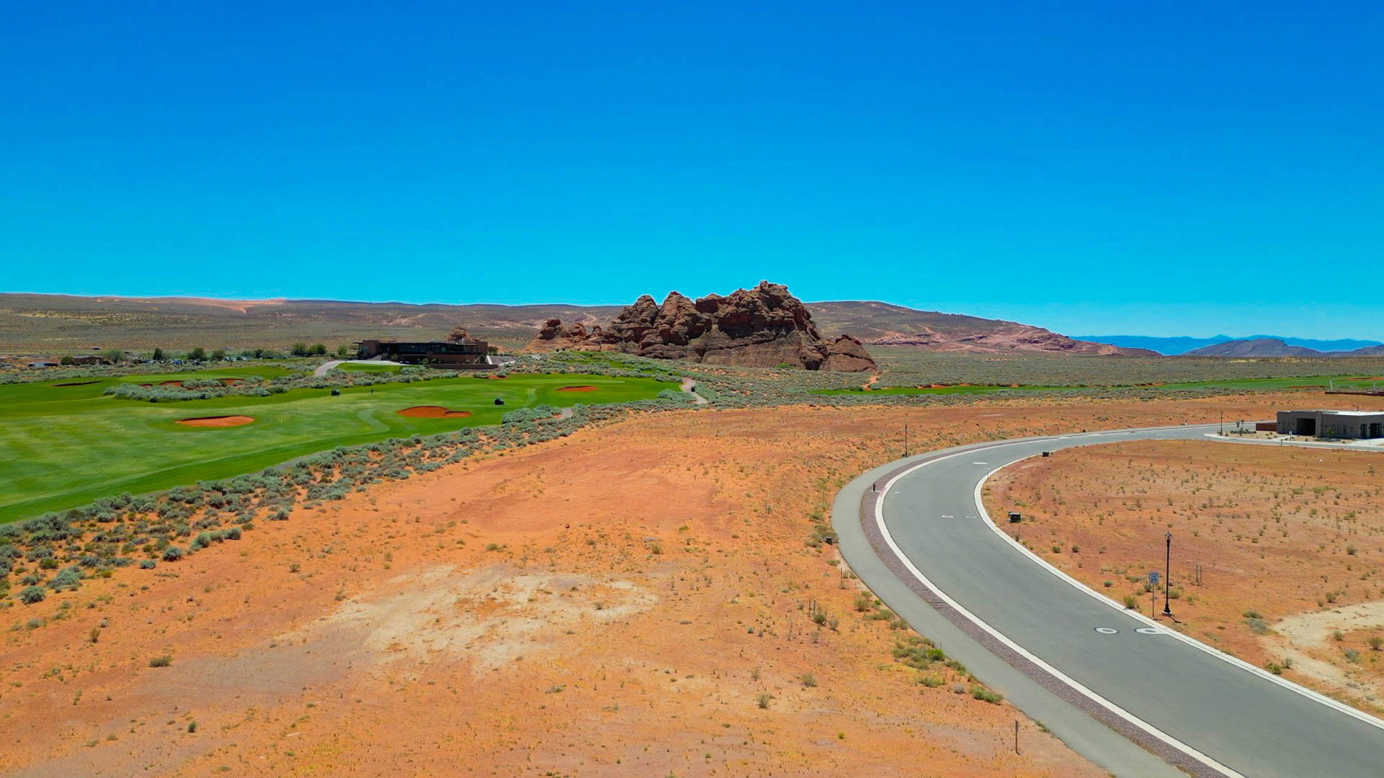 Expansive desert landscape featuring a paved road, natural rock formations, and a distant golf course with manicured greens