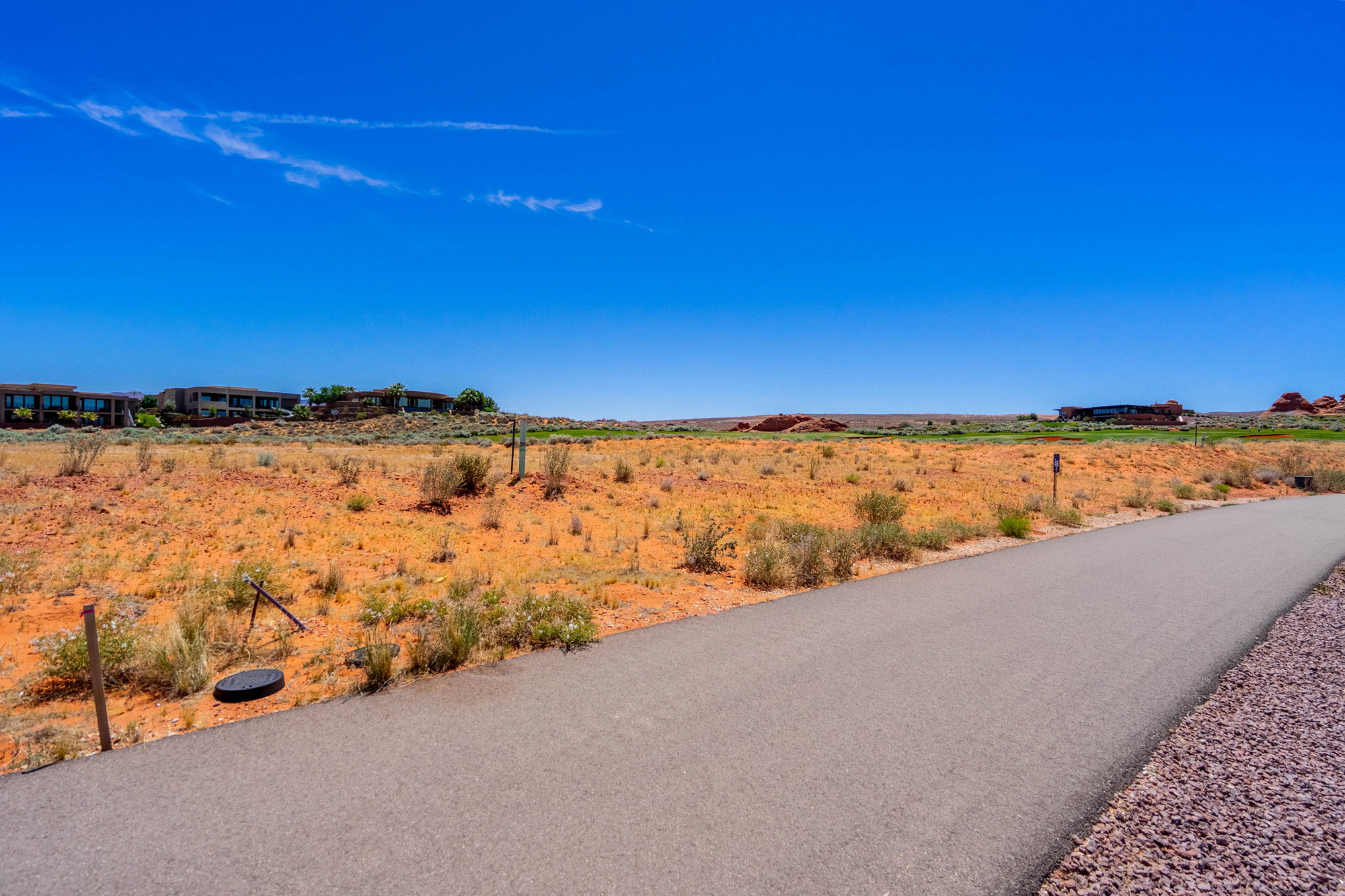 Paved pathway bordering an expansive undeveloped lot with natural desert landscaping
