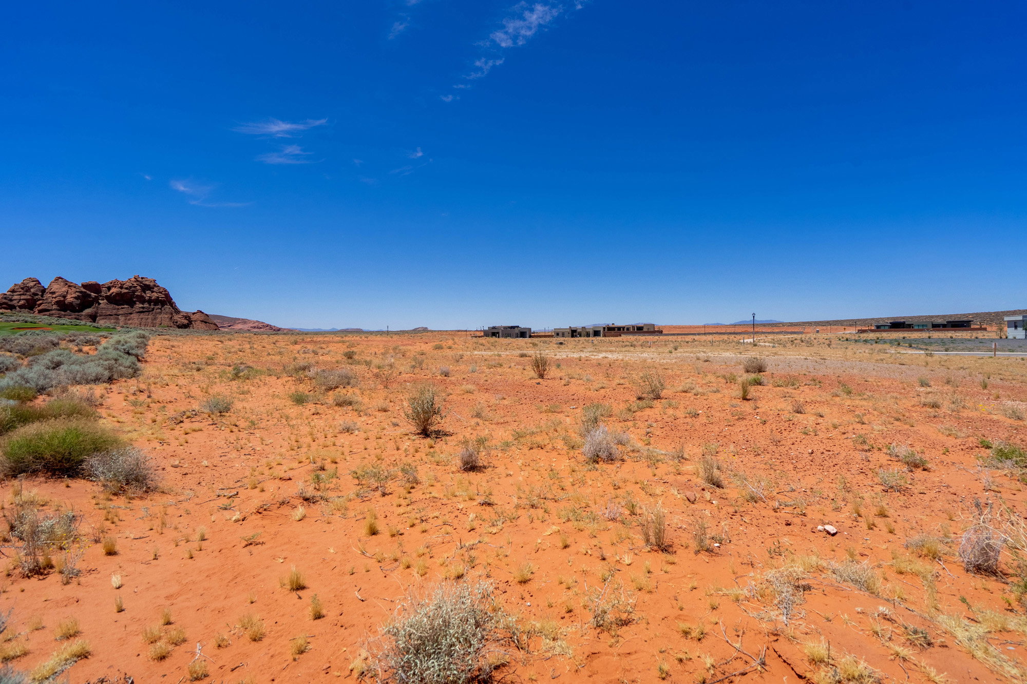 Expansive desert landscape featuring red earth, sparse low-lying vegetation, and distant rock formations